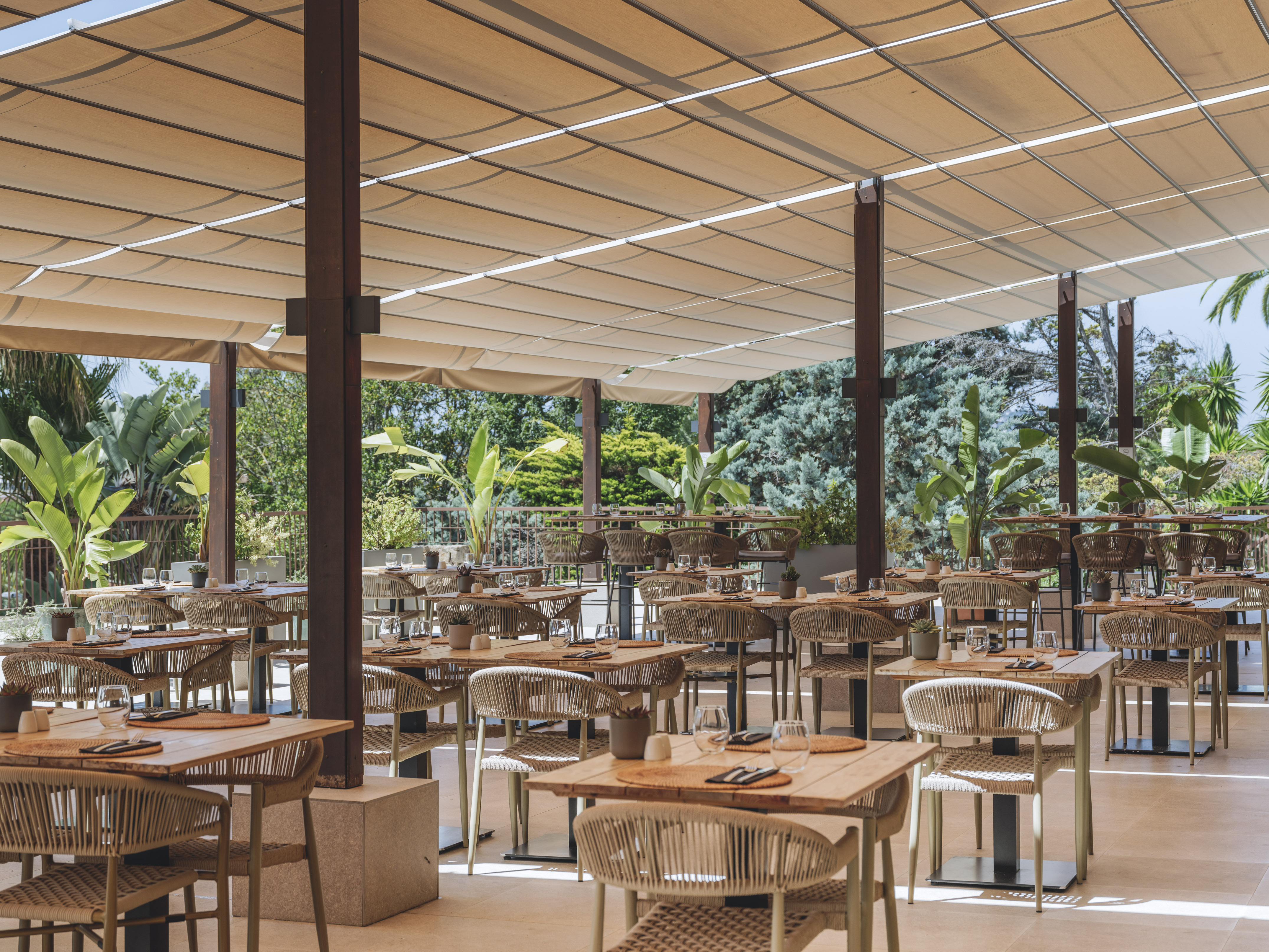 Shaded outdoor restaurant dining area with modern tables and lush greenery.