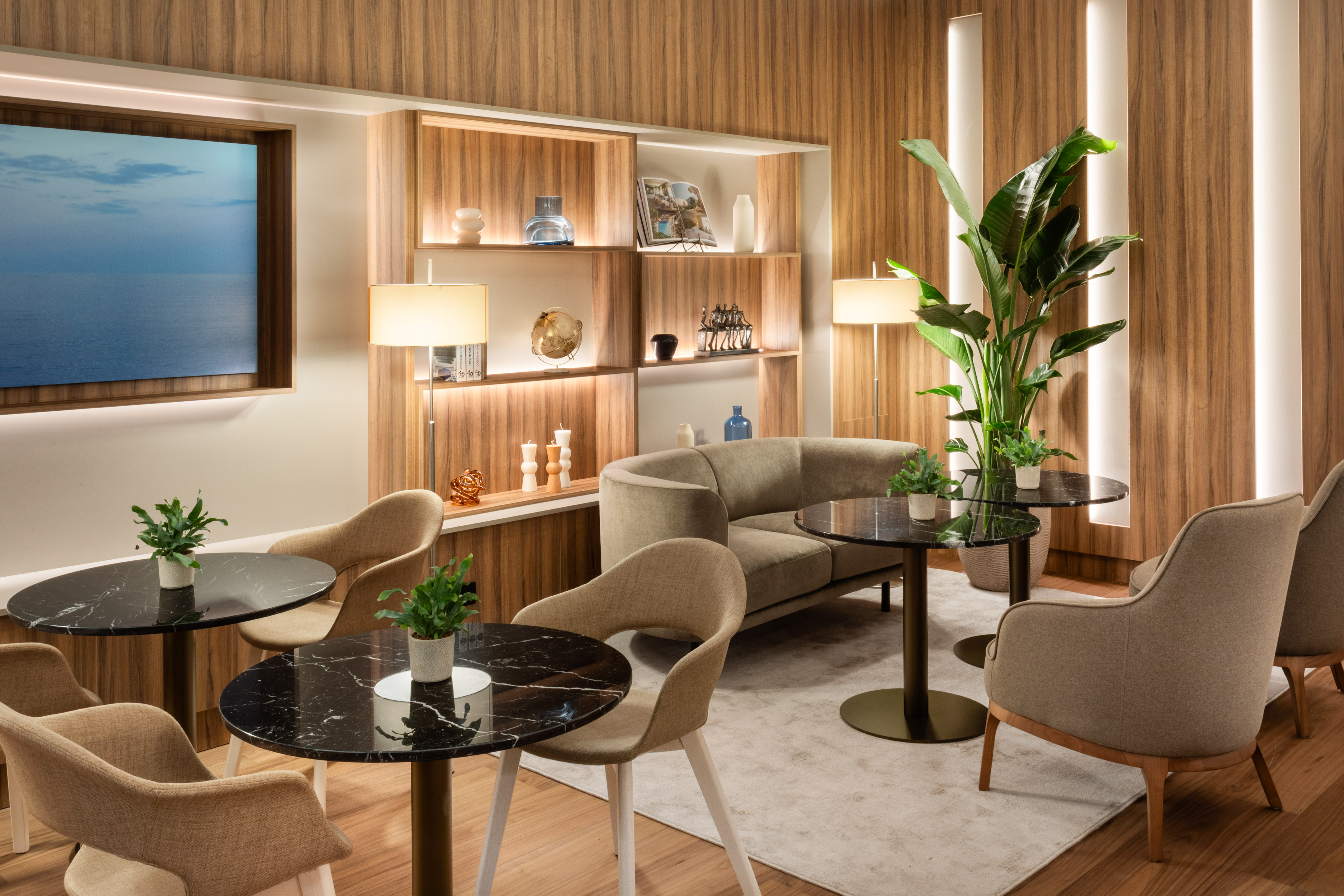 Modern lounge interior with wood panels, beige seating, marble tables, and plants.