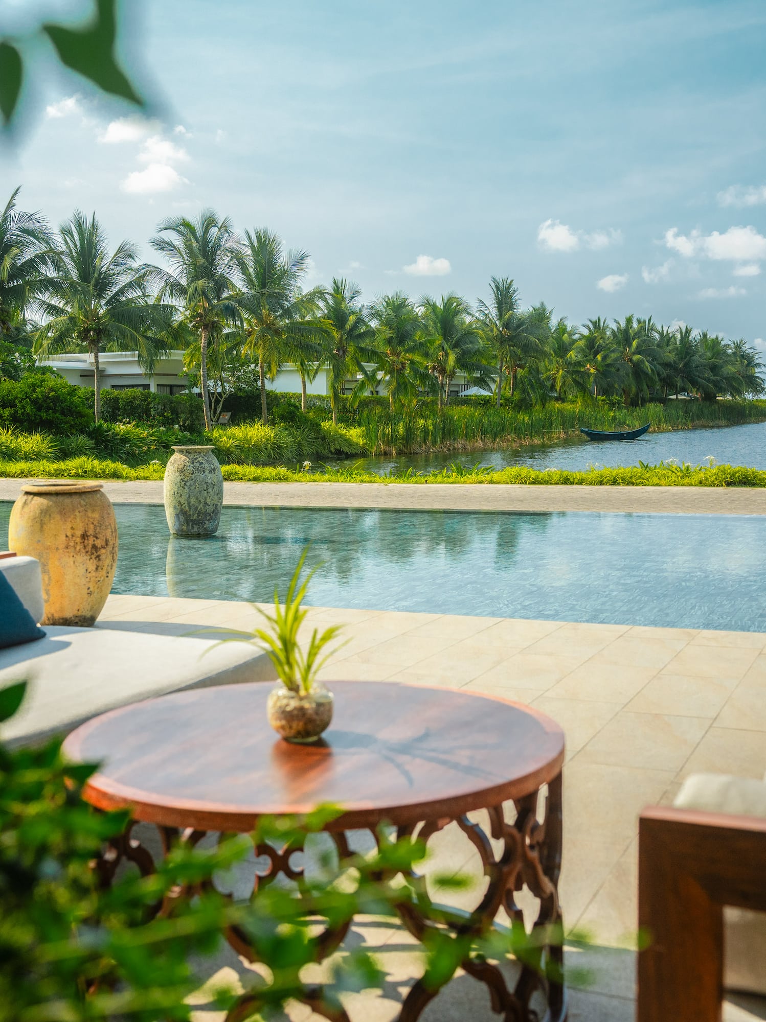 Tropical resort pool lounge with river view, palm trees, and boats.