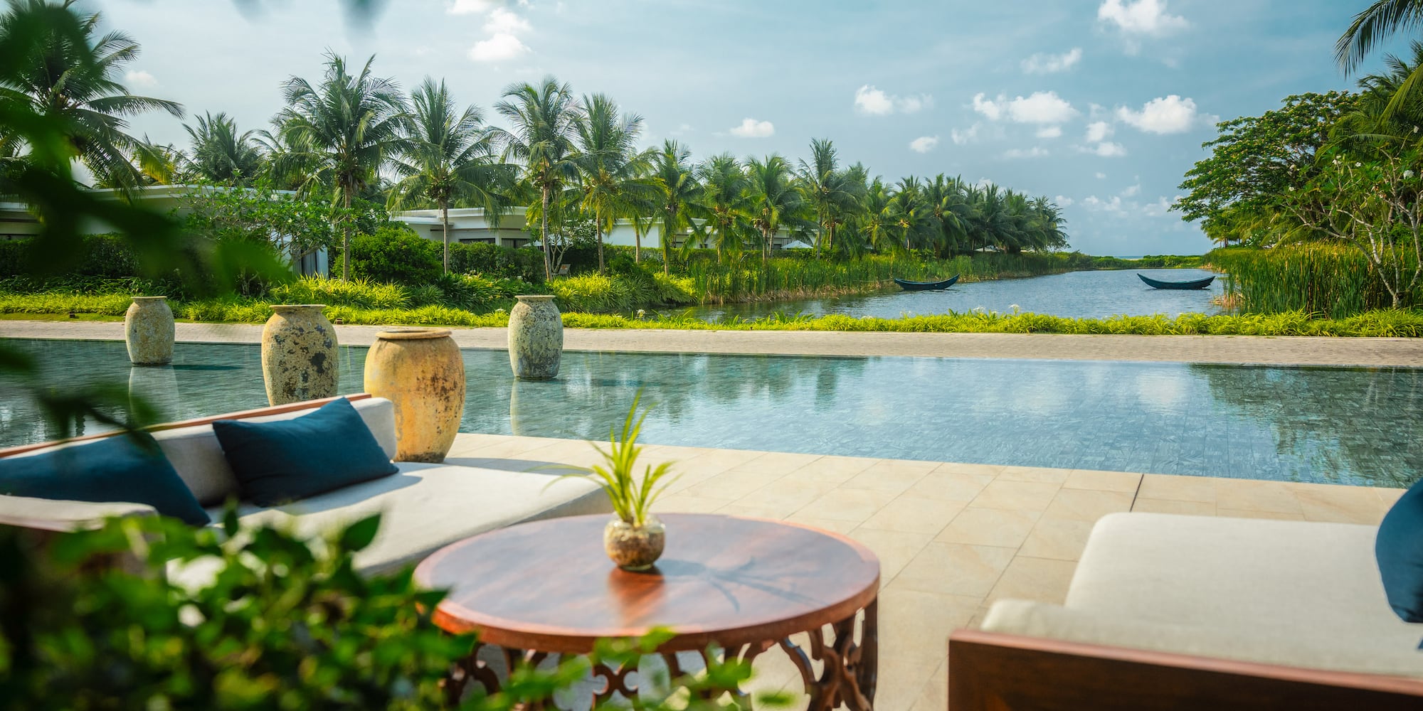 Tropical resort outdoor lounge with infinity pool, lake, and palm trees.