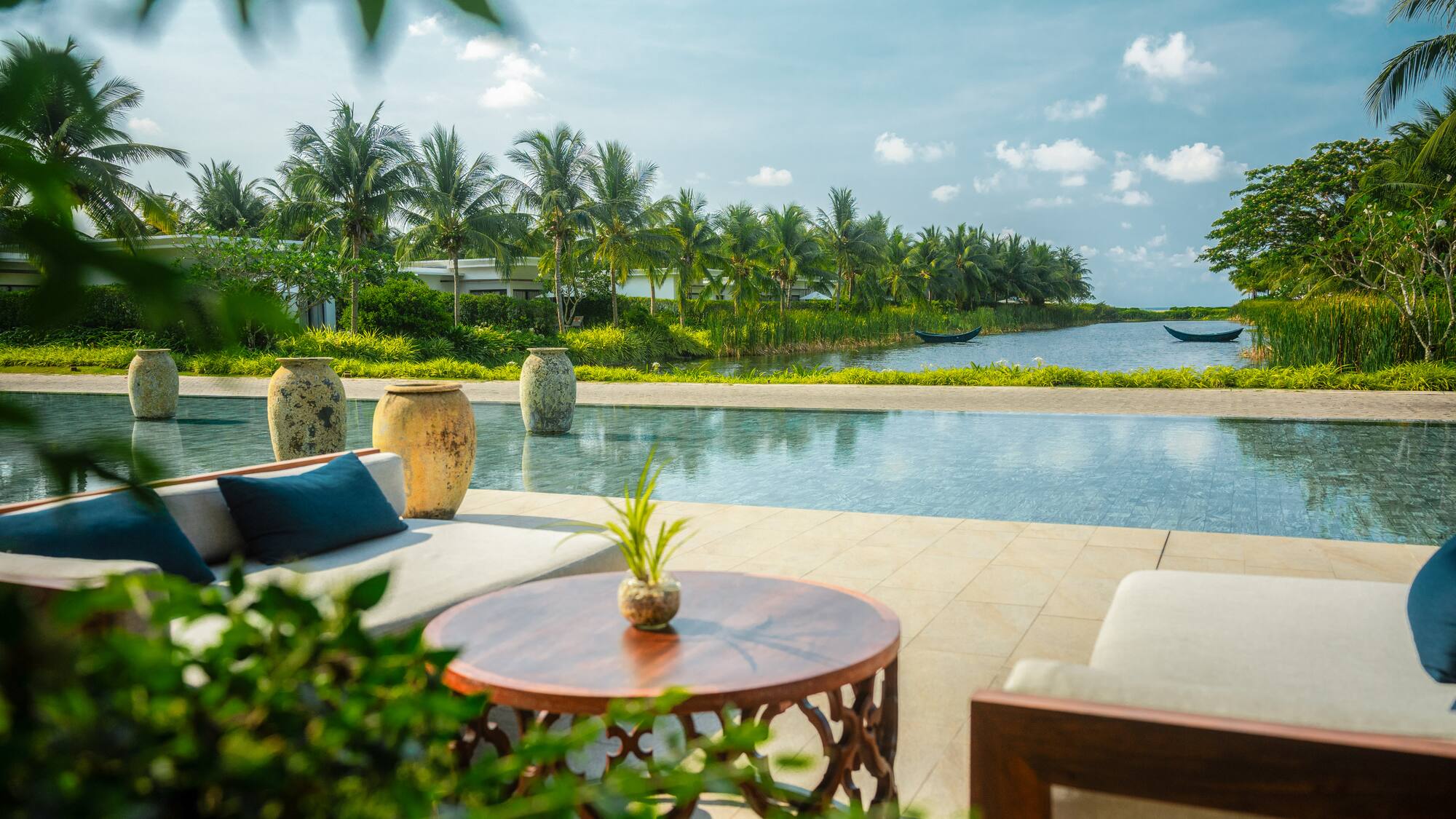 Tropical resort outdoor lounge with infinity pool, lake, and palm trees.