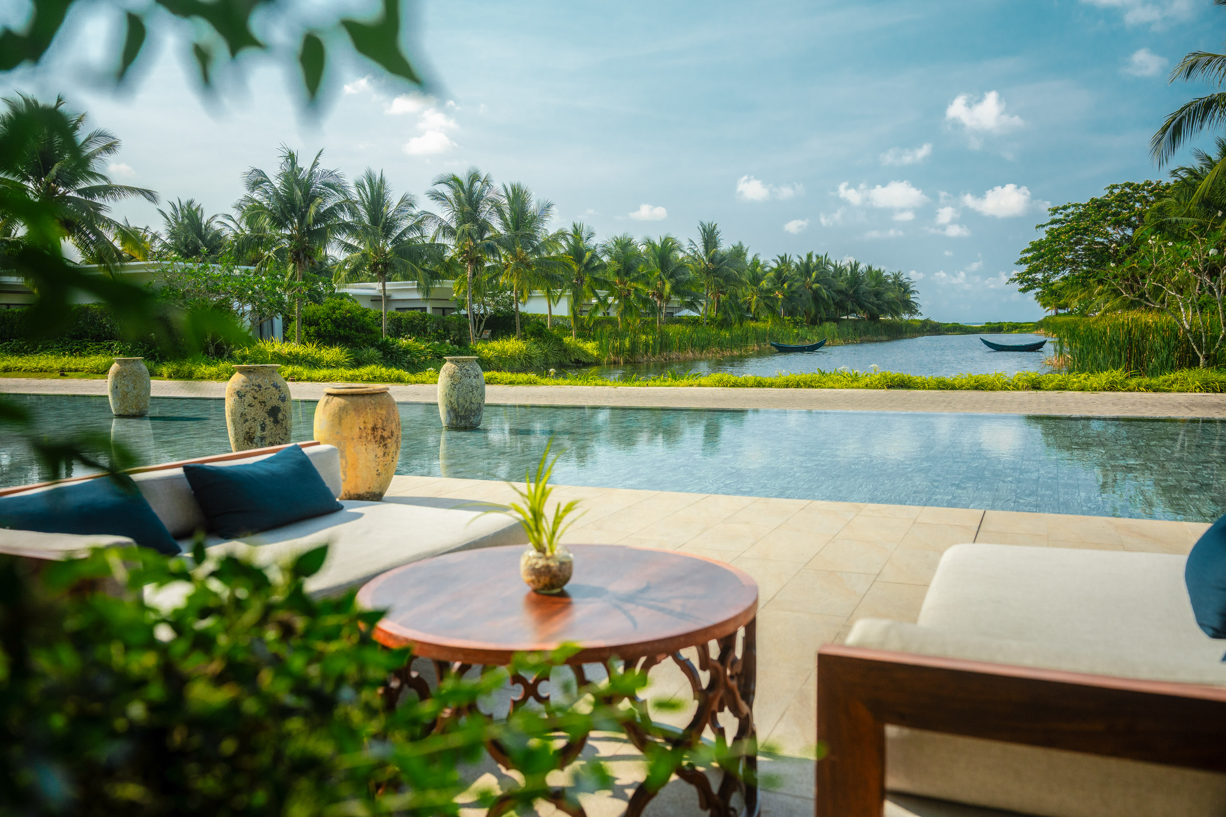 Tropical resort outdoor lounge with infinity pool, lake, and palm trees.