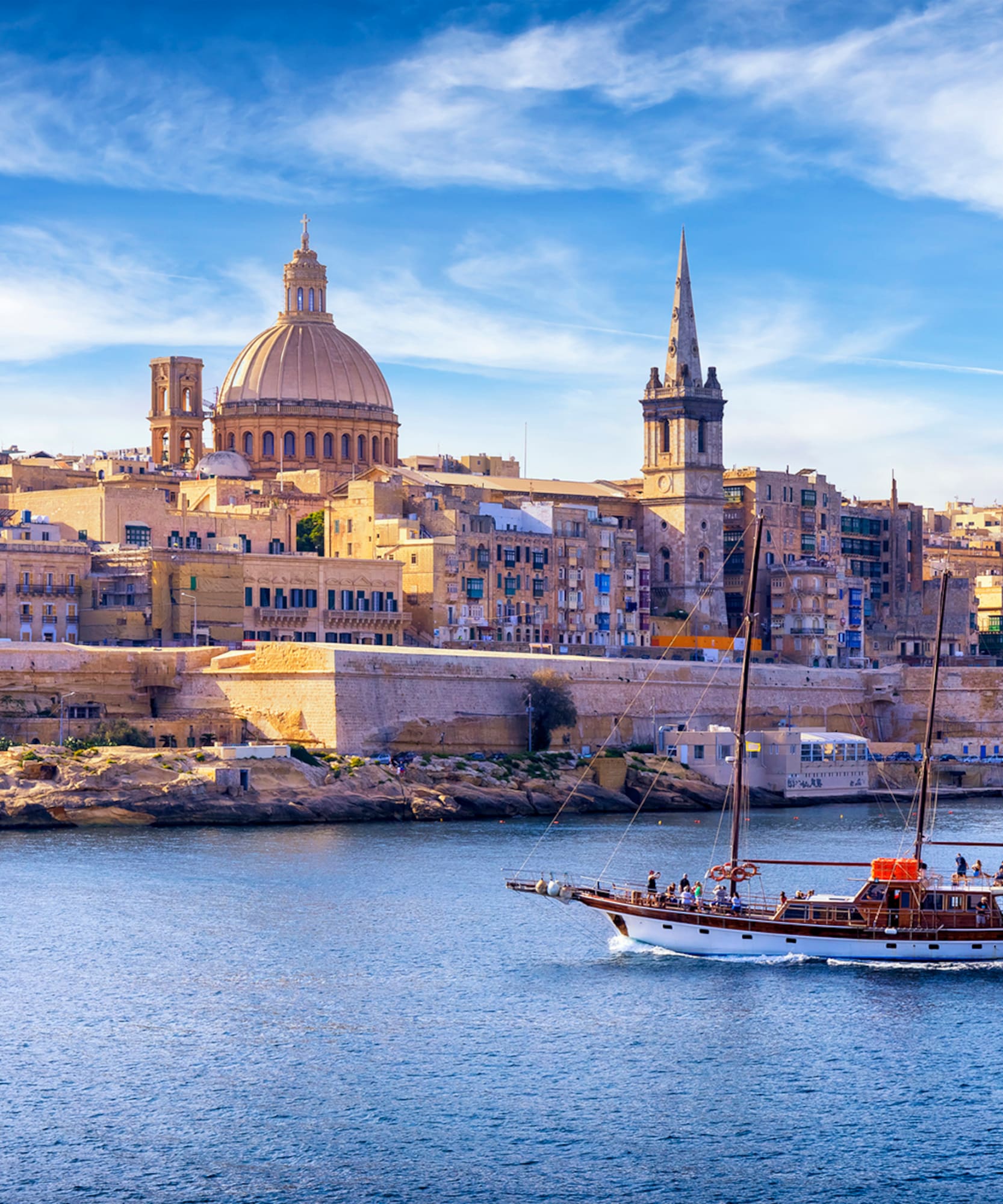 Valletta, Malta cityscape from water, with sailing boat, dome, and spire.