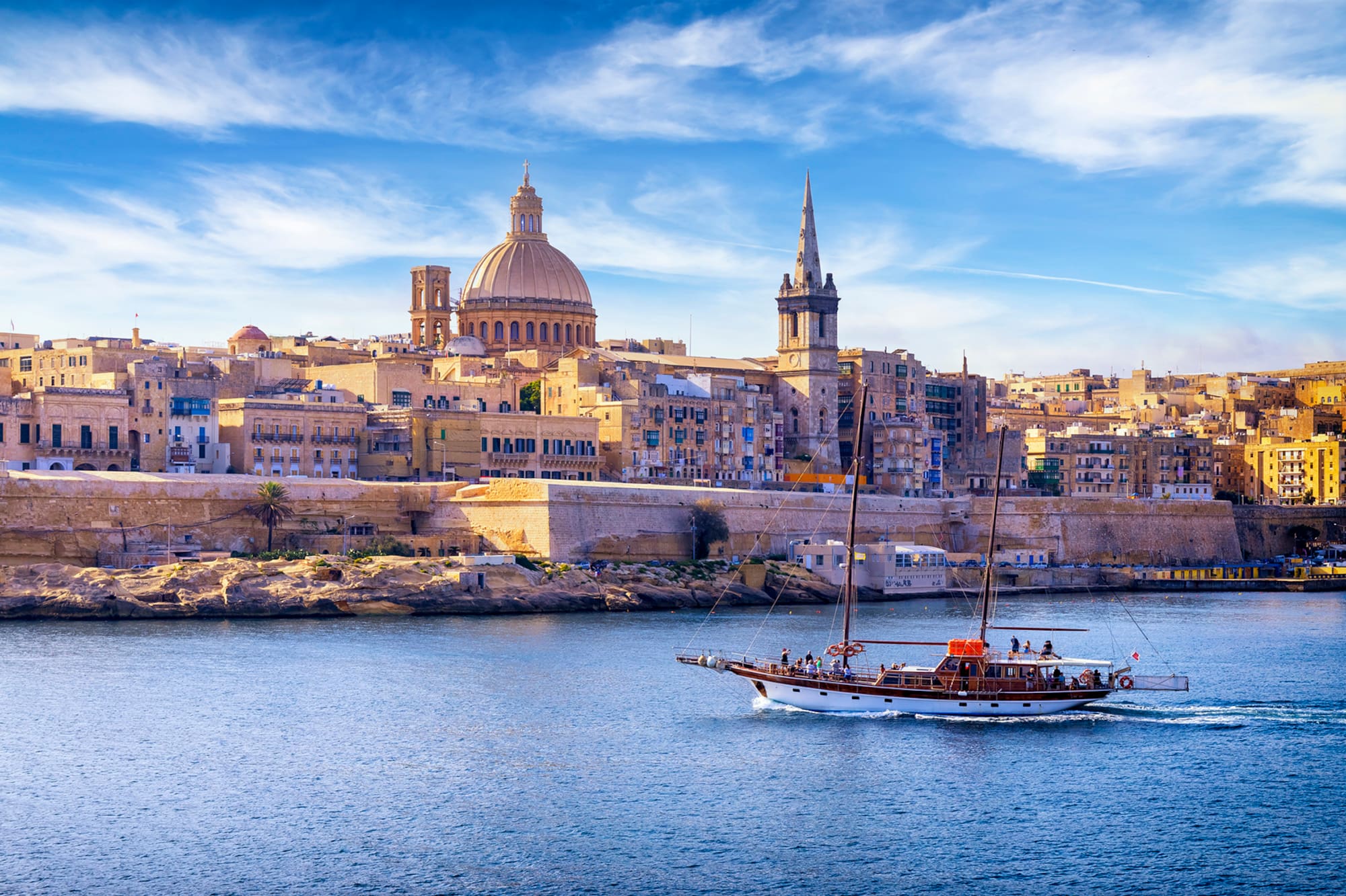 Valletta, Malta cityscape from water, with sailing boat, dome, and spire.