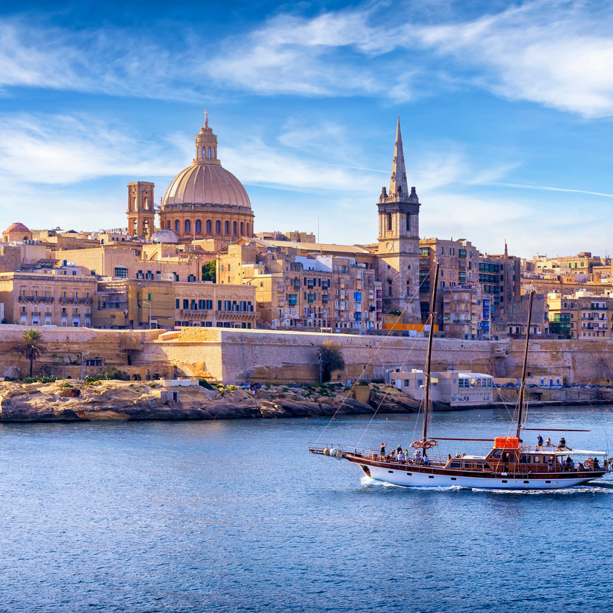 Valletta, Malta cityscape from water, with sailing boat, dome, and spire.