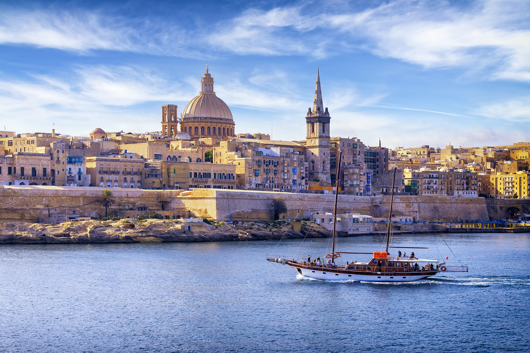 Valletta, Malta cityscape from water, with sailing boat, dome, and spire.