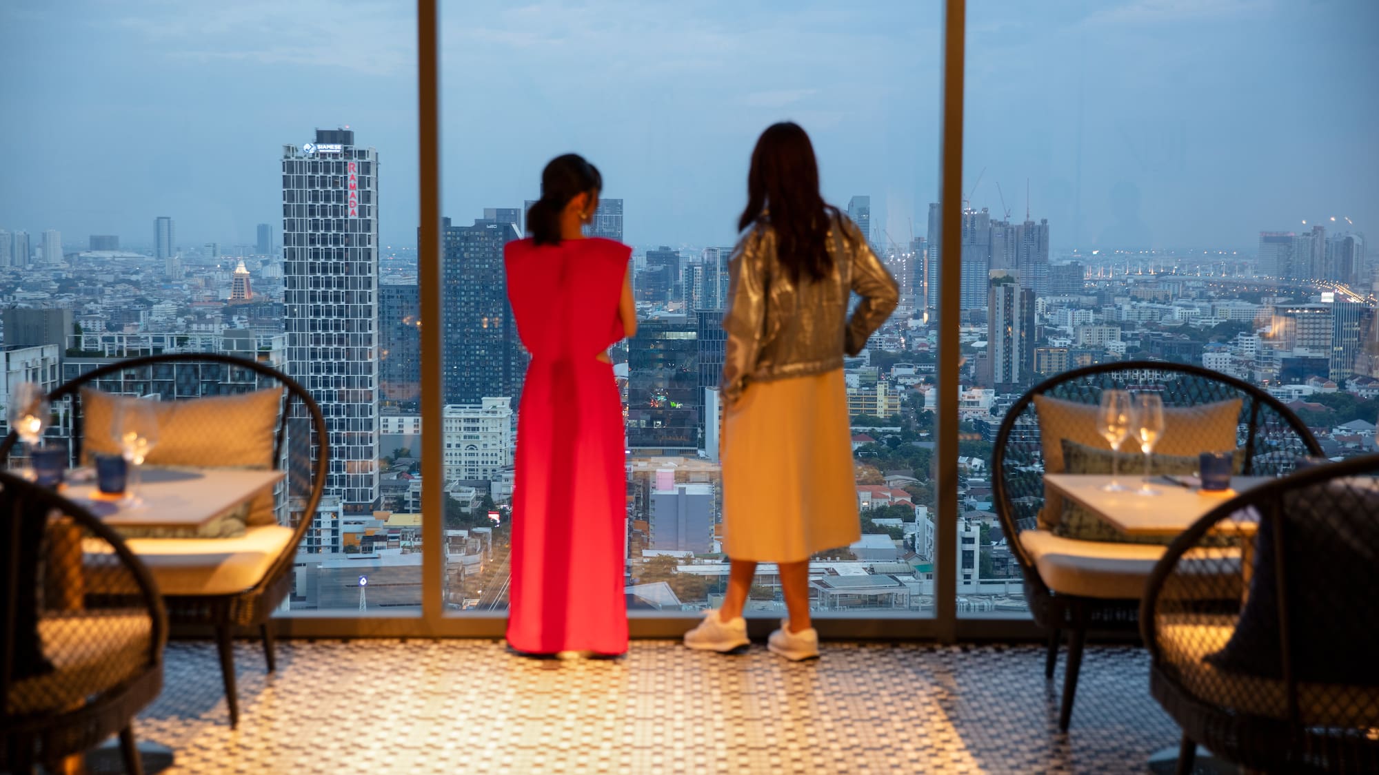 two women looking out a window at a city