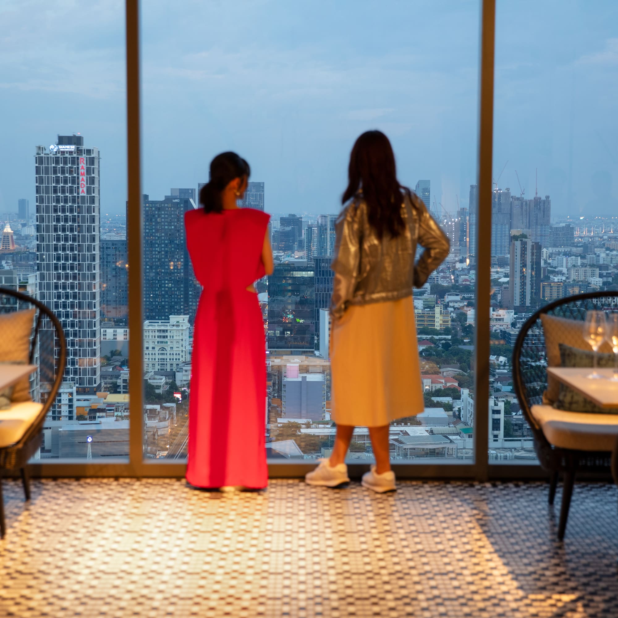 two women looking out a window at a city