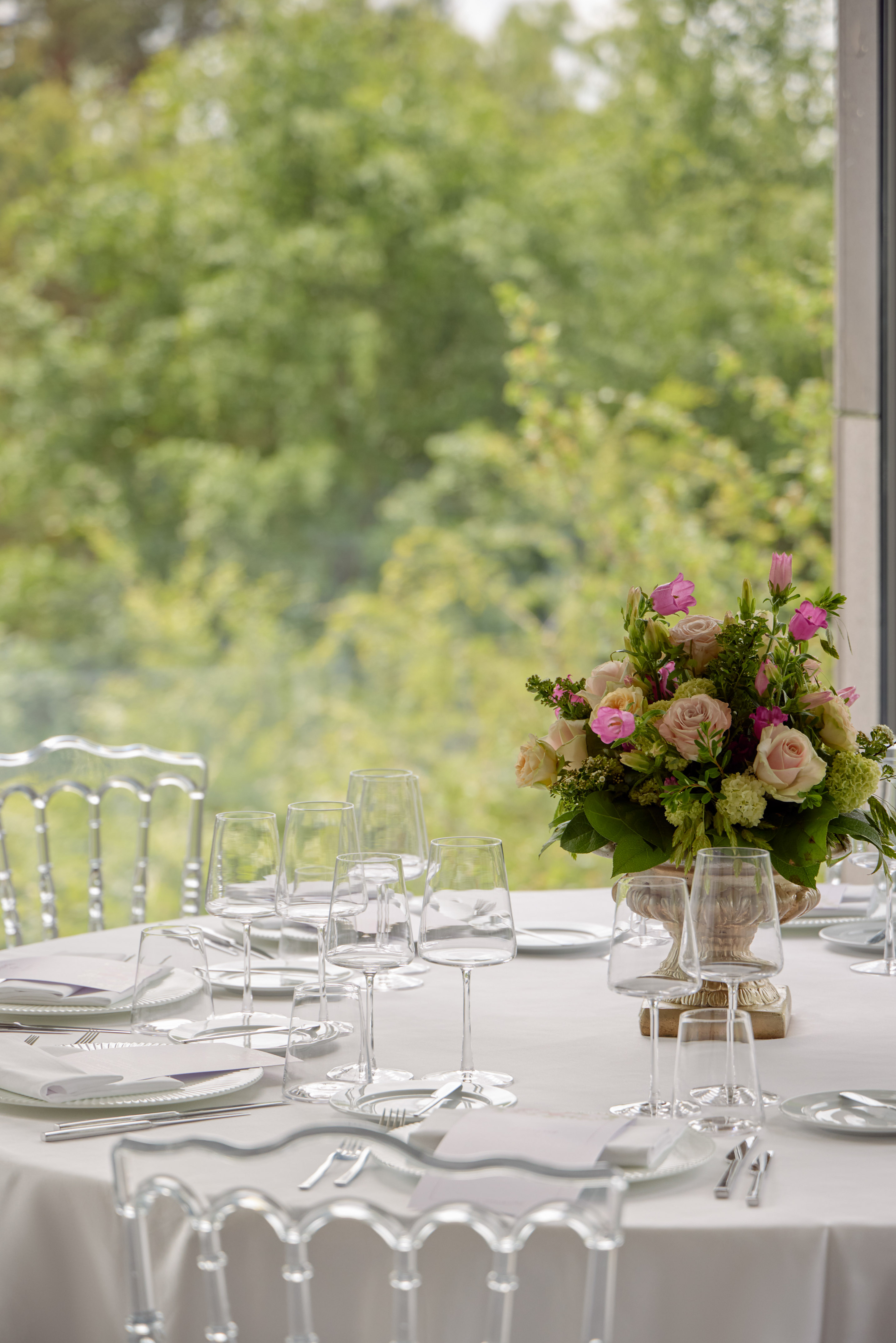 Elegant table set for wedding with floral centerpiece, clear chairs, outdoor view.