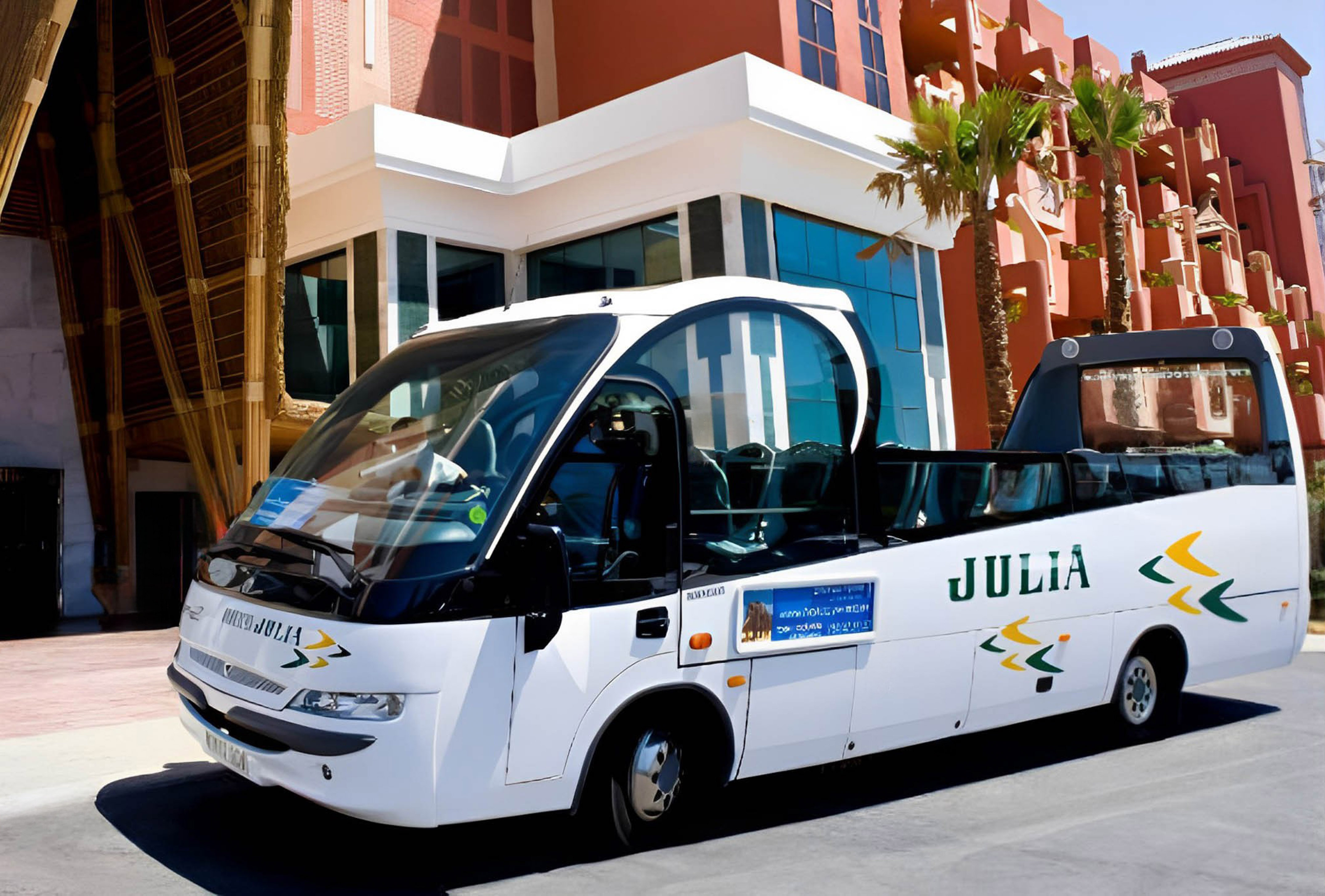 White Julia open-top sightseeing bus at modern hotel resort with palm trees.