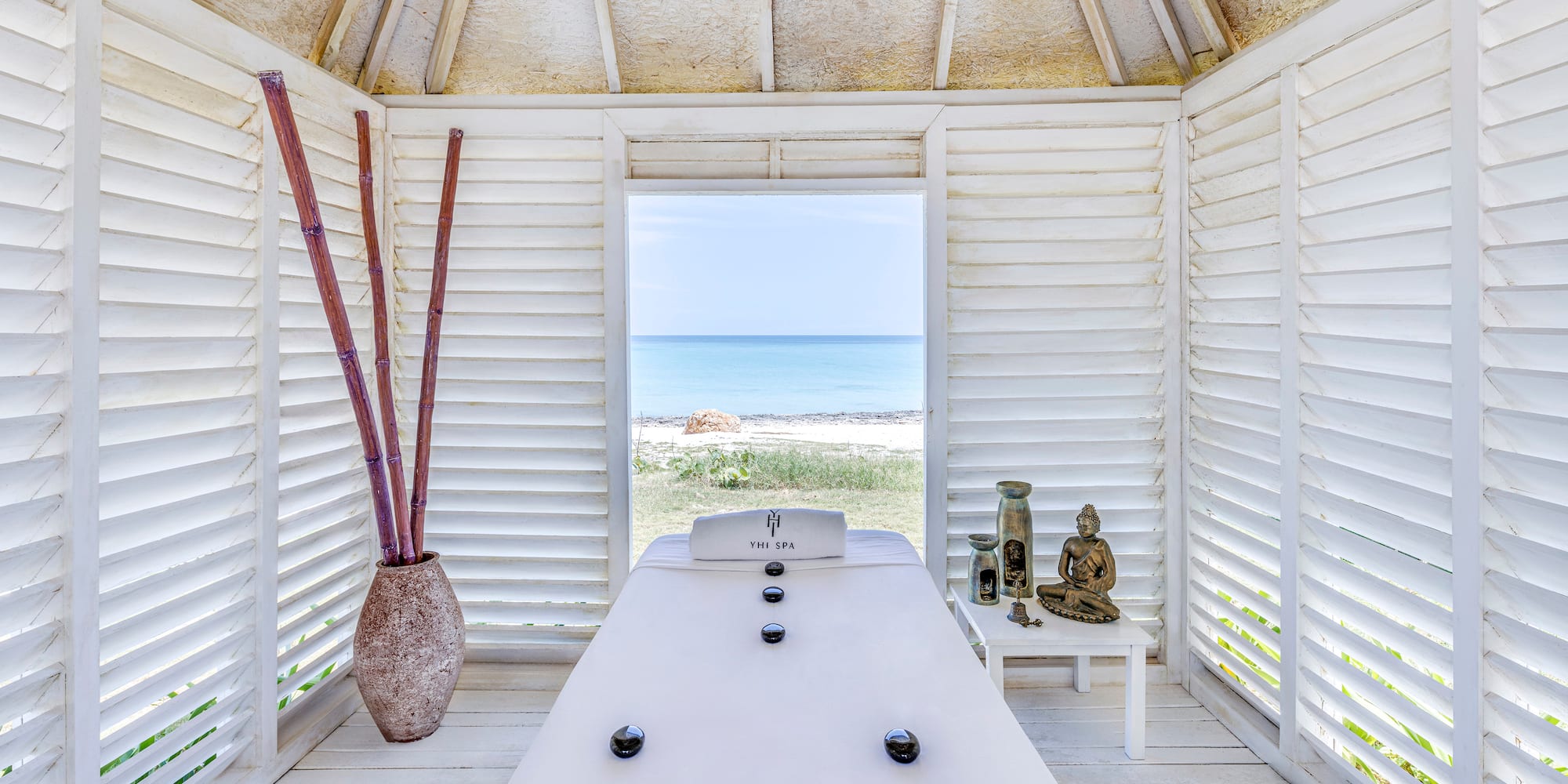 a room with a white table and a vase of bamboo and a beach view