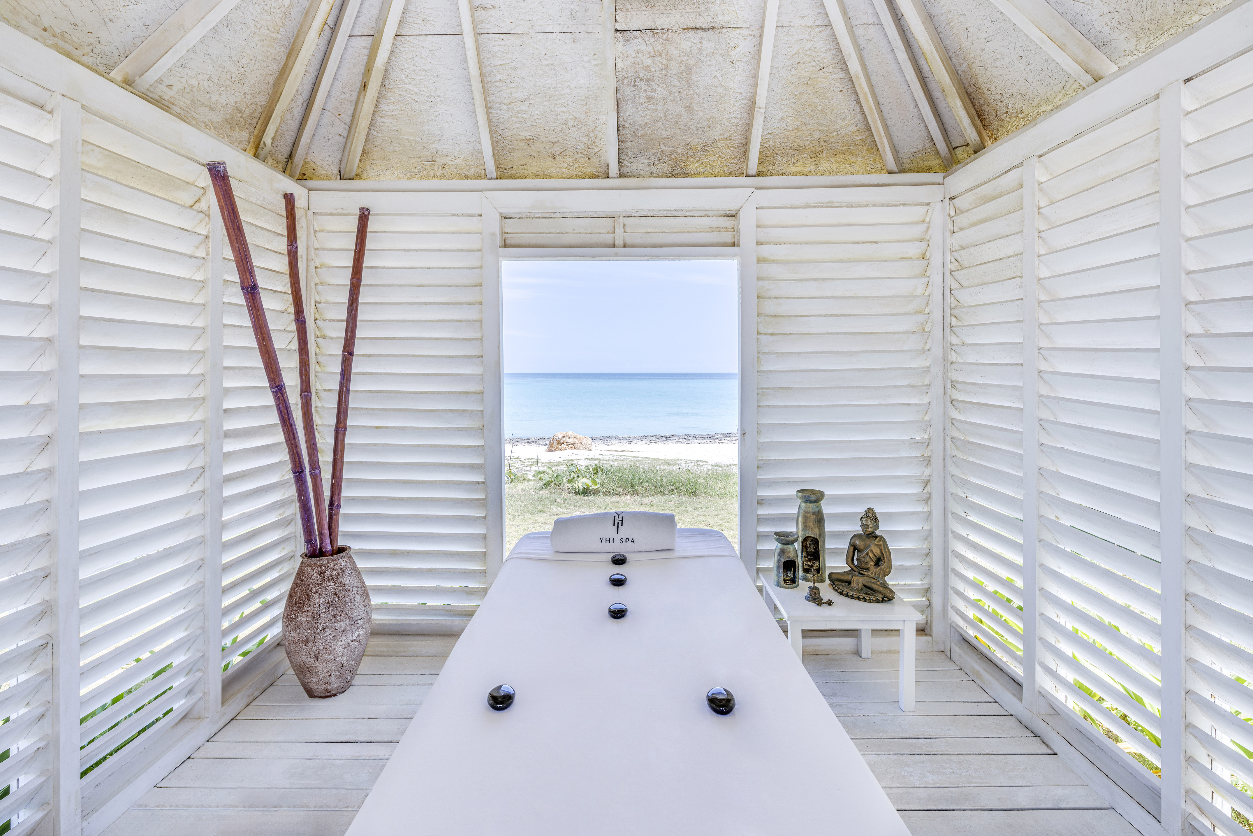 a room with a white table and a vase of bamboo and a beach view