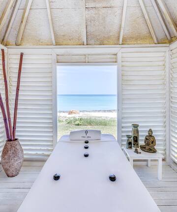 a room with a white table and a vase of bamboo and a beach view