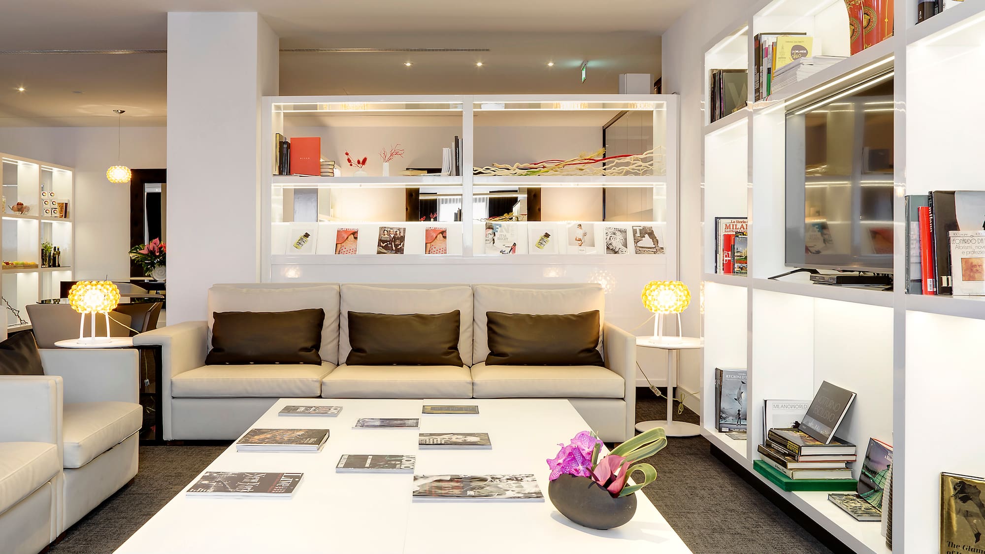 Bright hotel lounge with white sofa, coffee table, and illuminated display shelves.