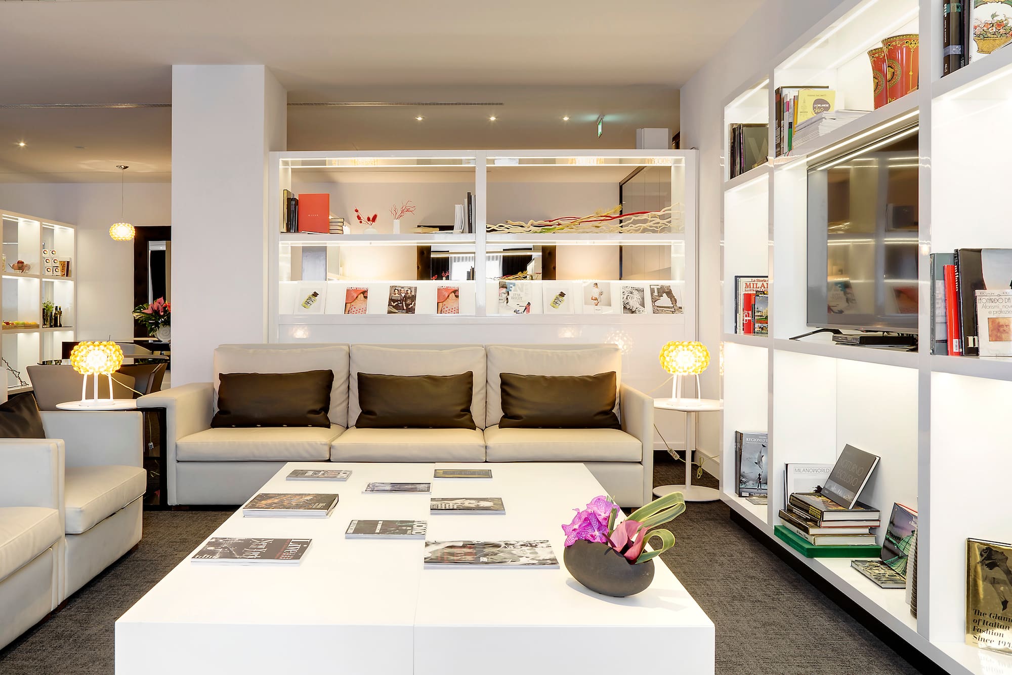 Bright hotel lounge with white sofa, coffee table, and illuminated display shelves.