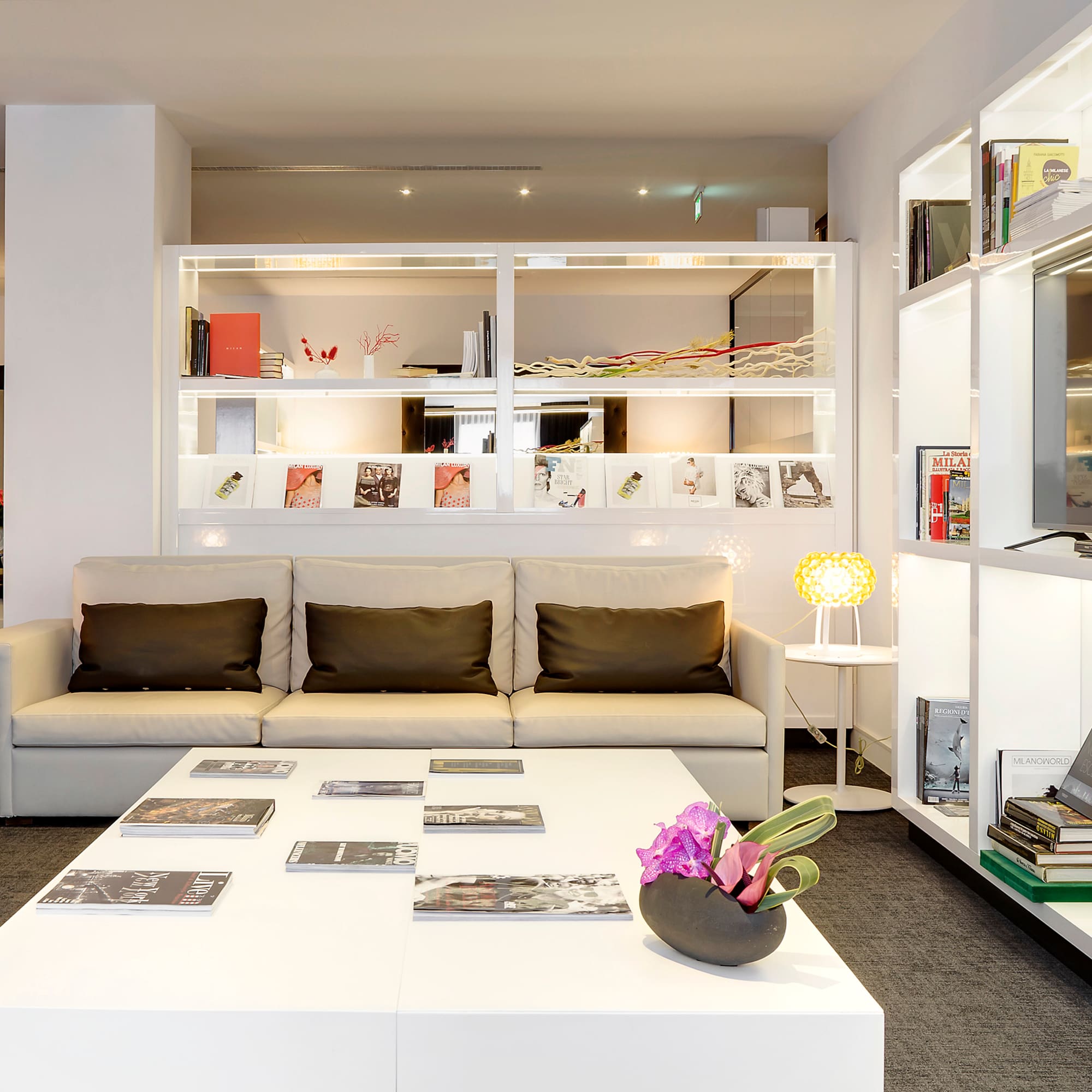 Bright hotel lounge with white sofa, coffee table, and illuminated display shelves.
