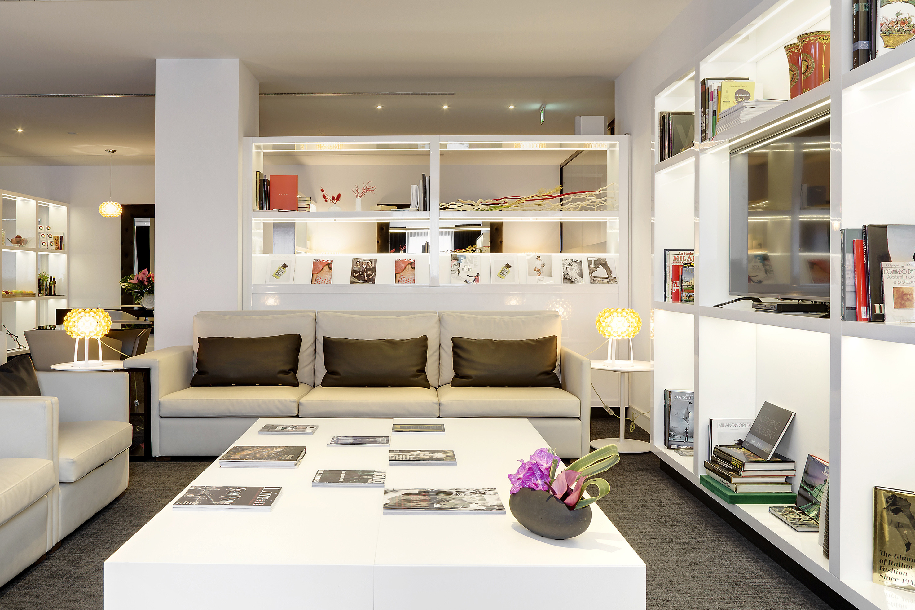 Contemporary lounge with cream sofas, white coffee table, and illuminated shelves.