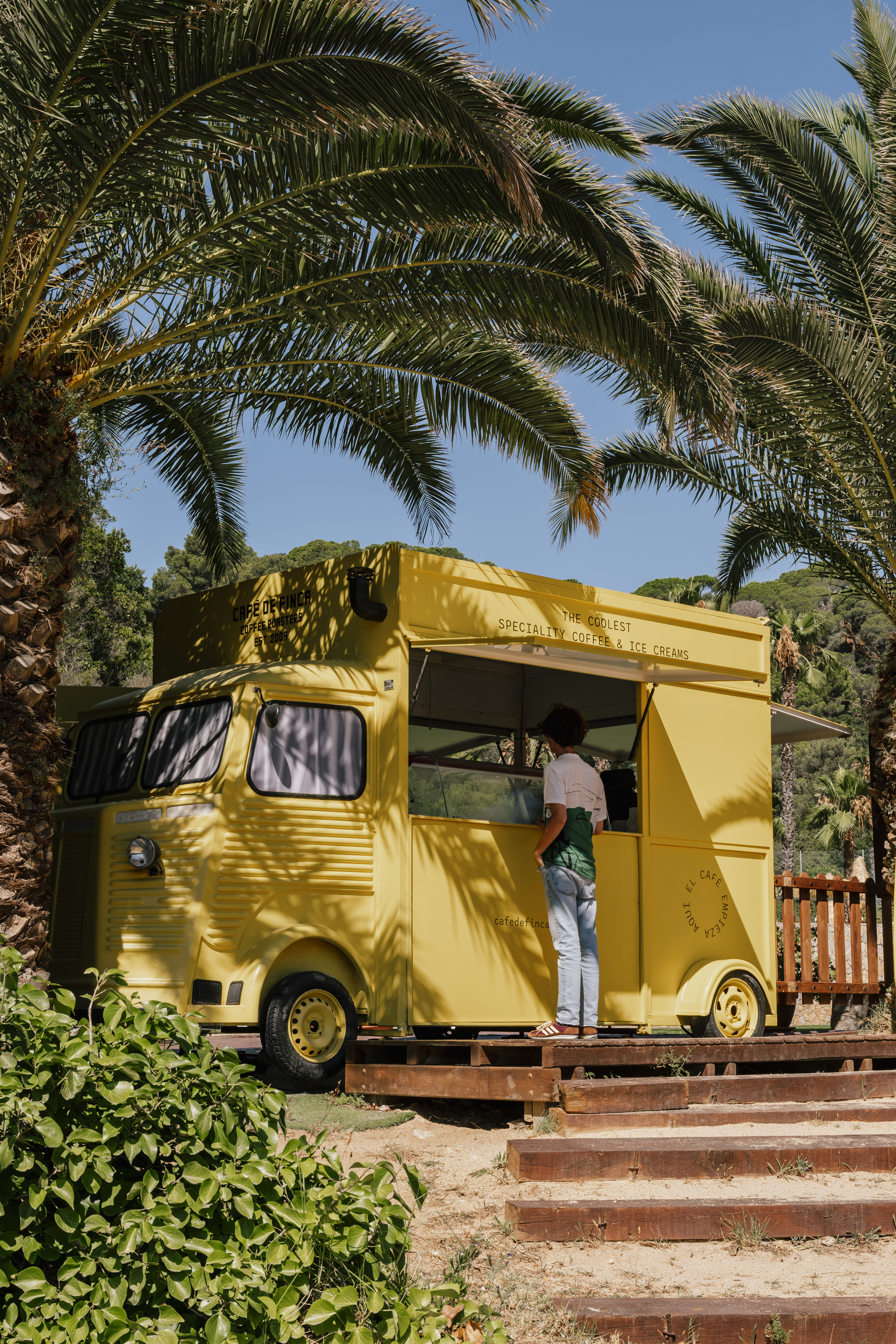 Yellow Cafe de Finca coffee and ice cream food truck under palm trees.