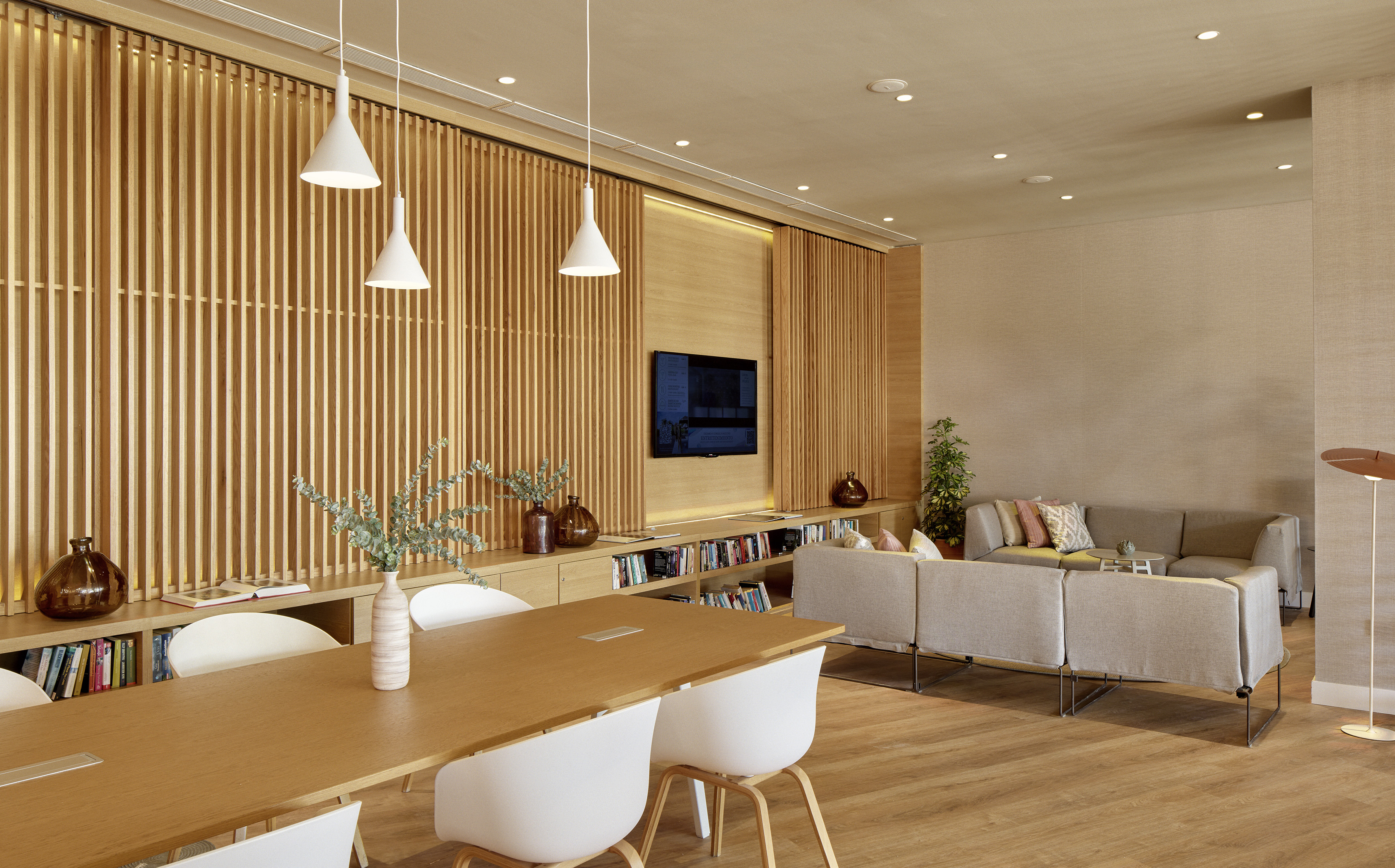 Contemporary lounge with wooden wall, long meeting table, and seating area.