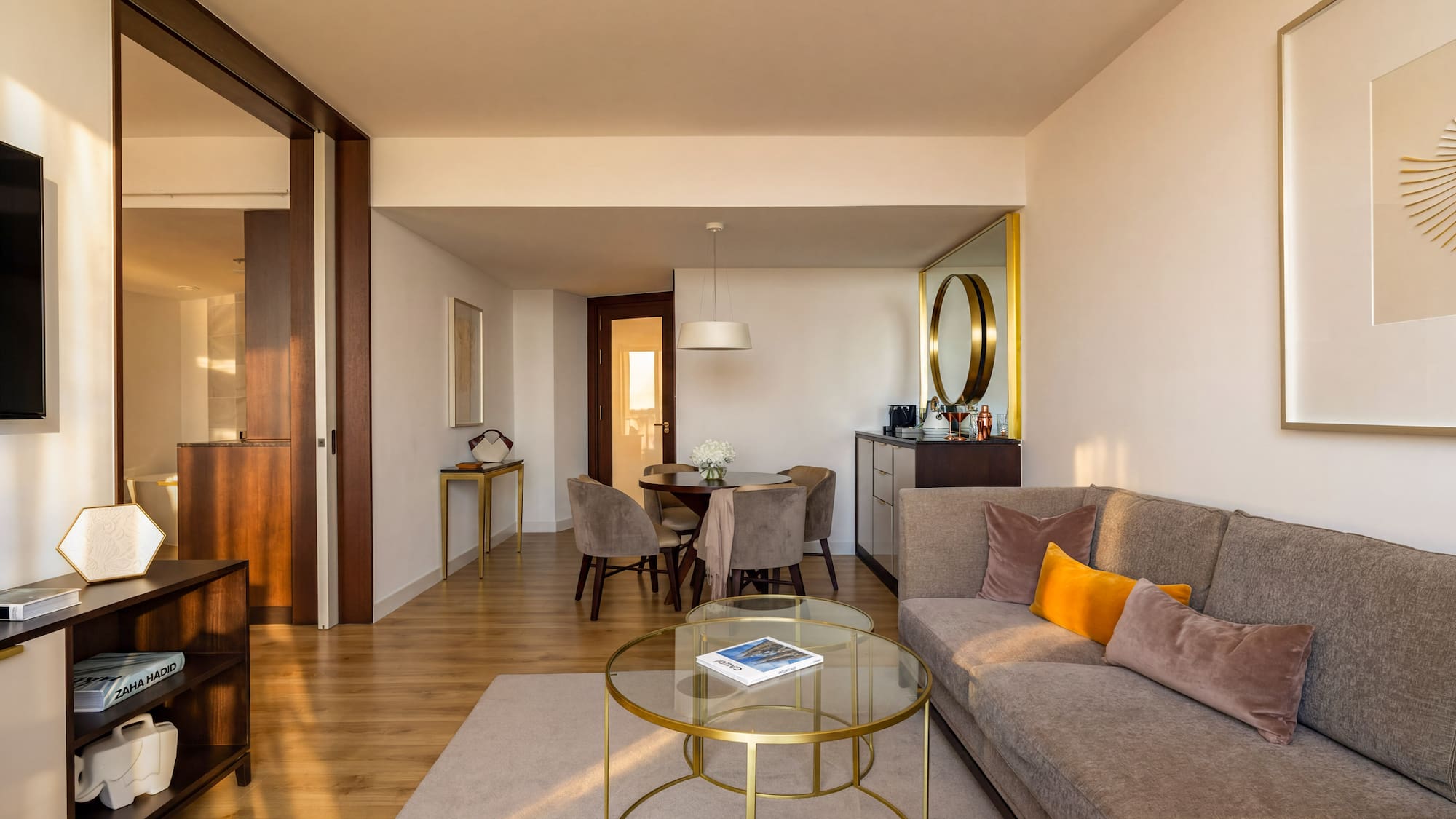 Modern hotel suite living room with dining area, gray sofa, and wood floors.
