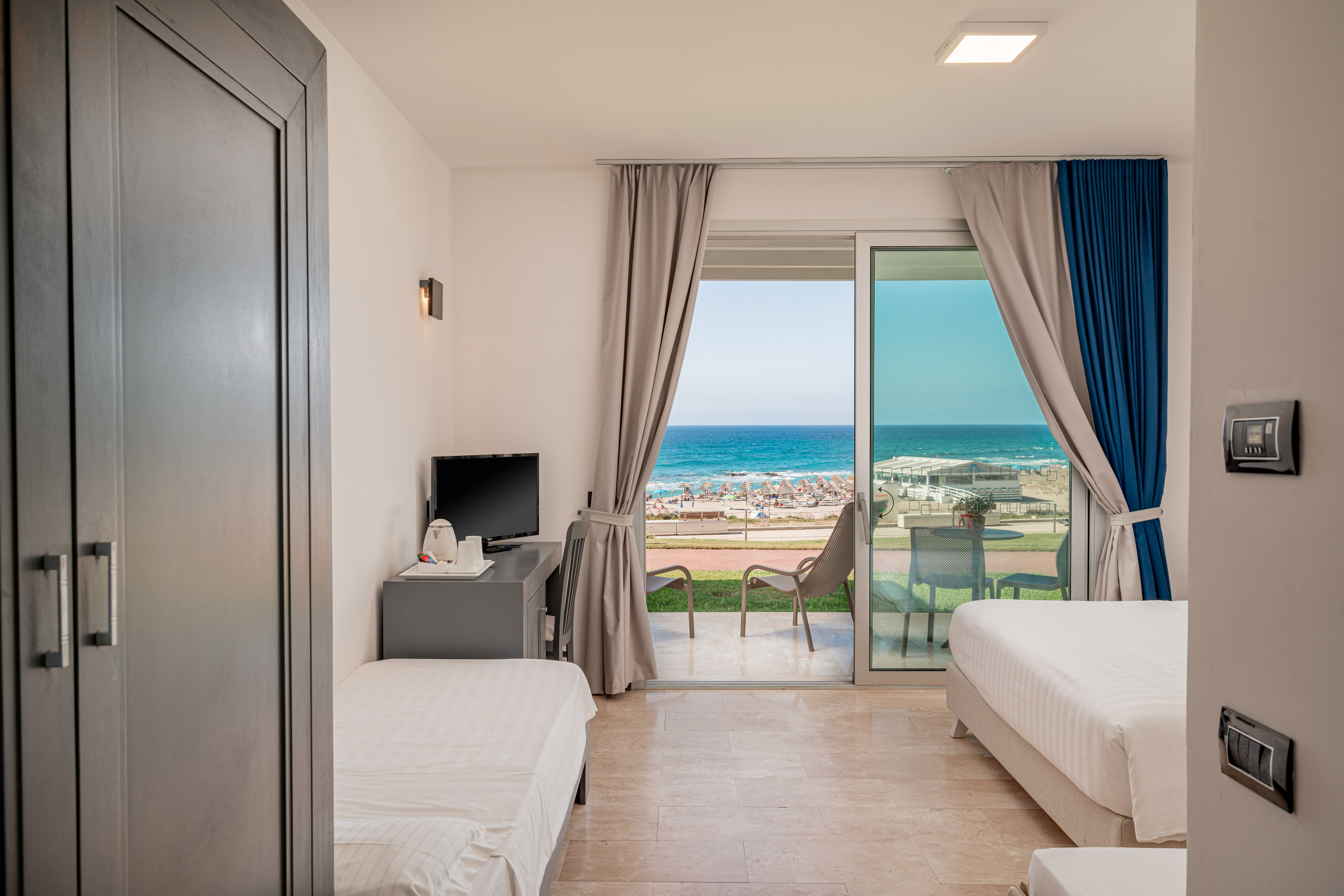 Hotel room with beds, desk, balcony, and clear ocean and beach view.