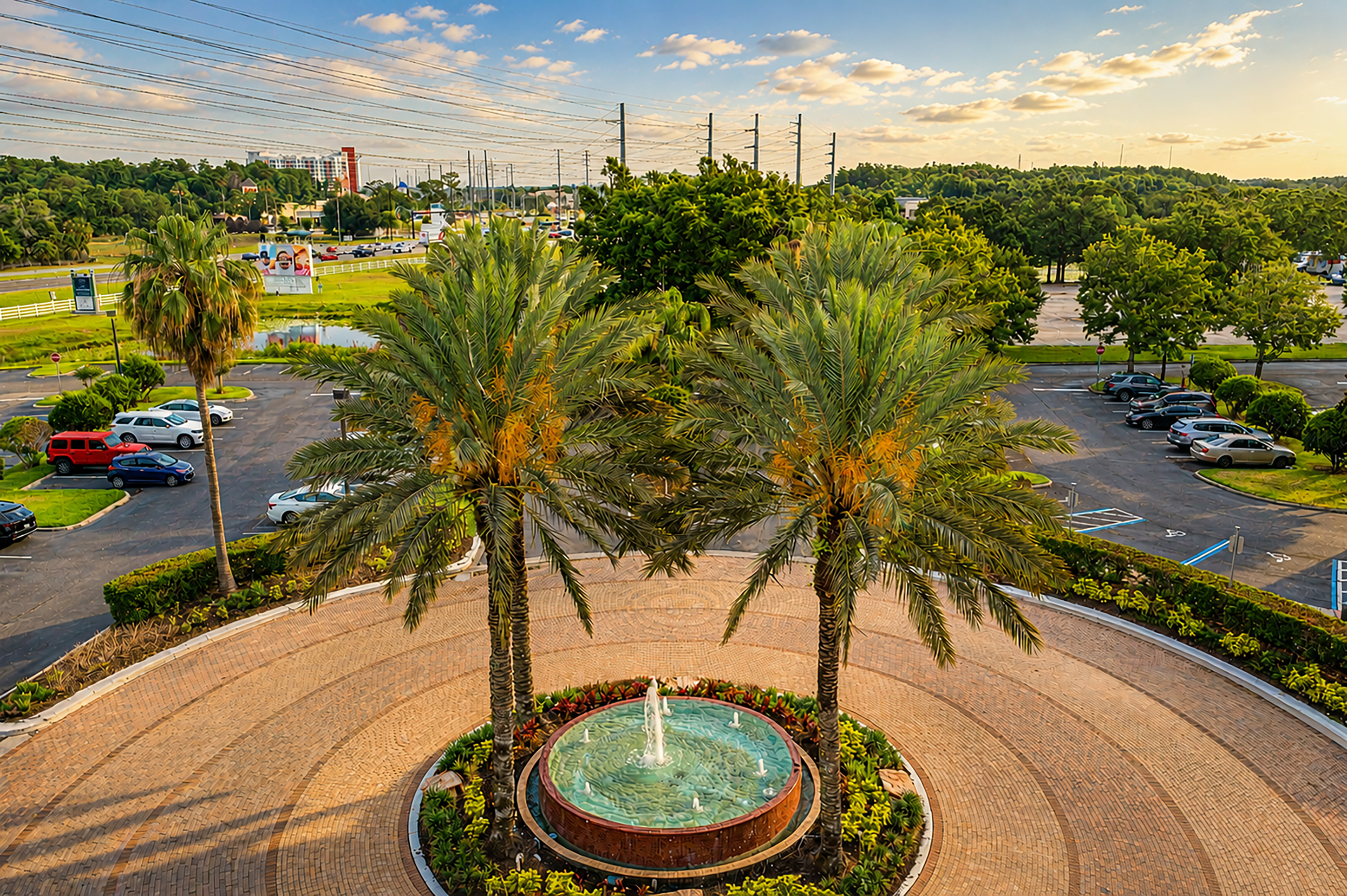 Tropical resort entrance with fountain, twin palm trees, and brick driveway.