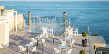 a patio with white tables and chairs and a fountain in front of the ocean