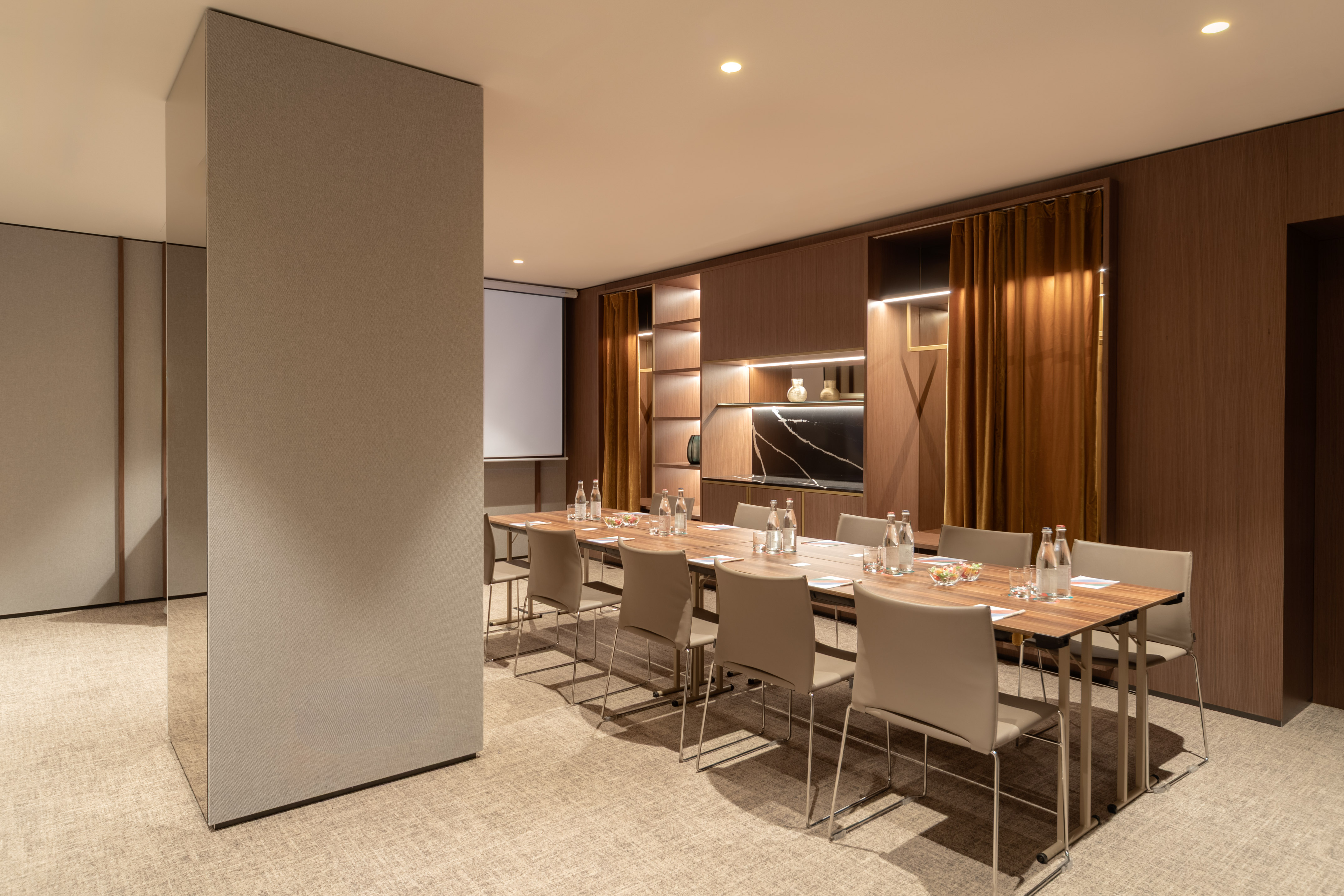 Modern conference room with long table, chairs, projector screen, and warm wood interior.