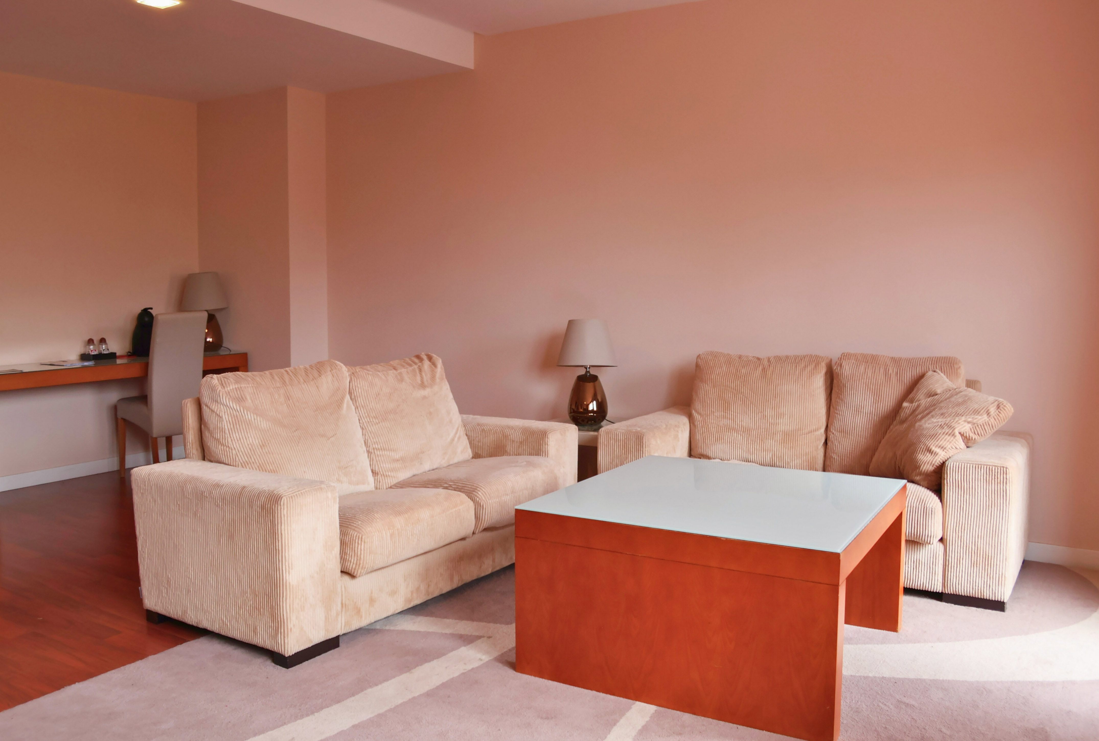 Modern living room with beige corduroy sofas, orange coffee table, and desk.