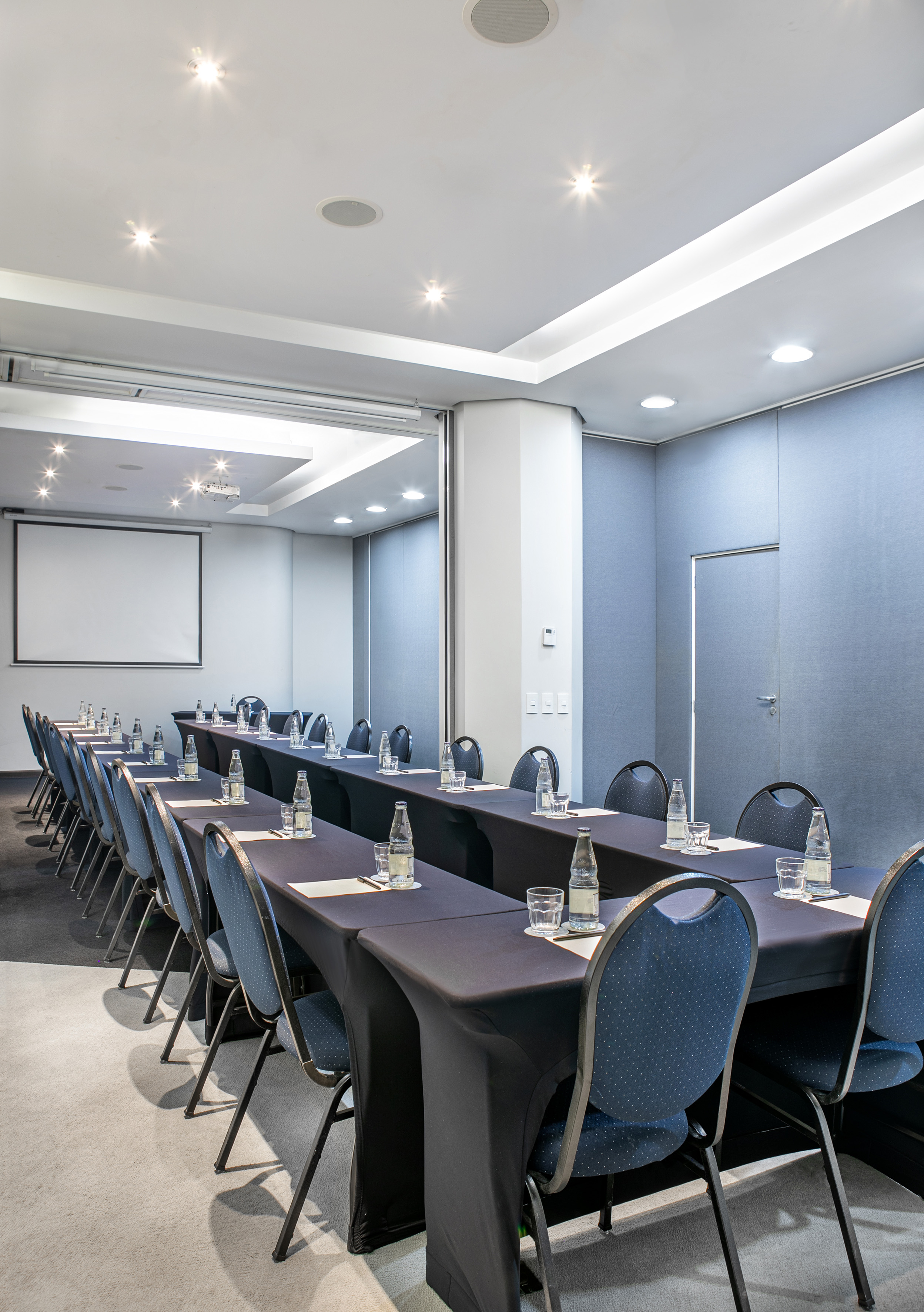 Bright meeting room with tables, chairs, and screen for presentations.