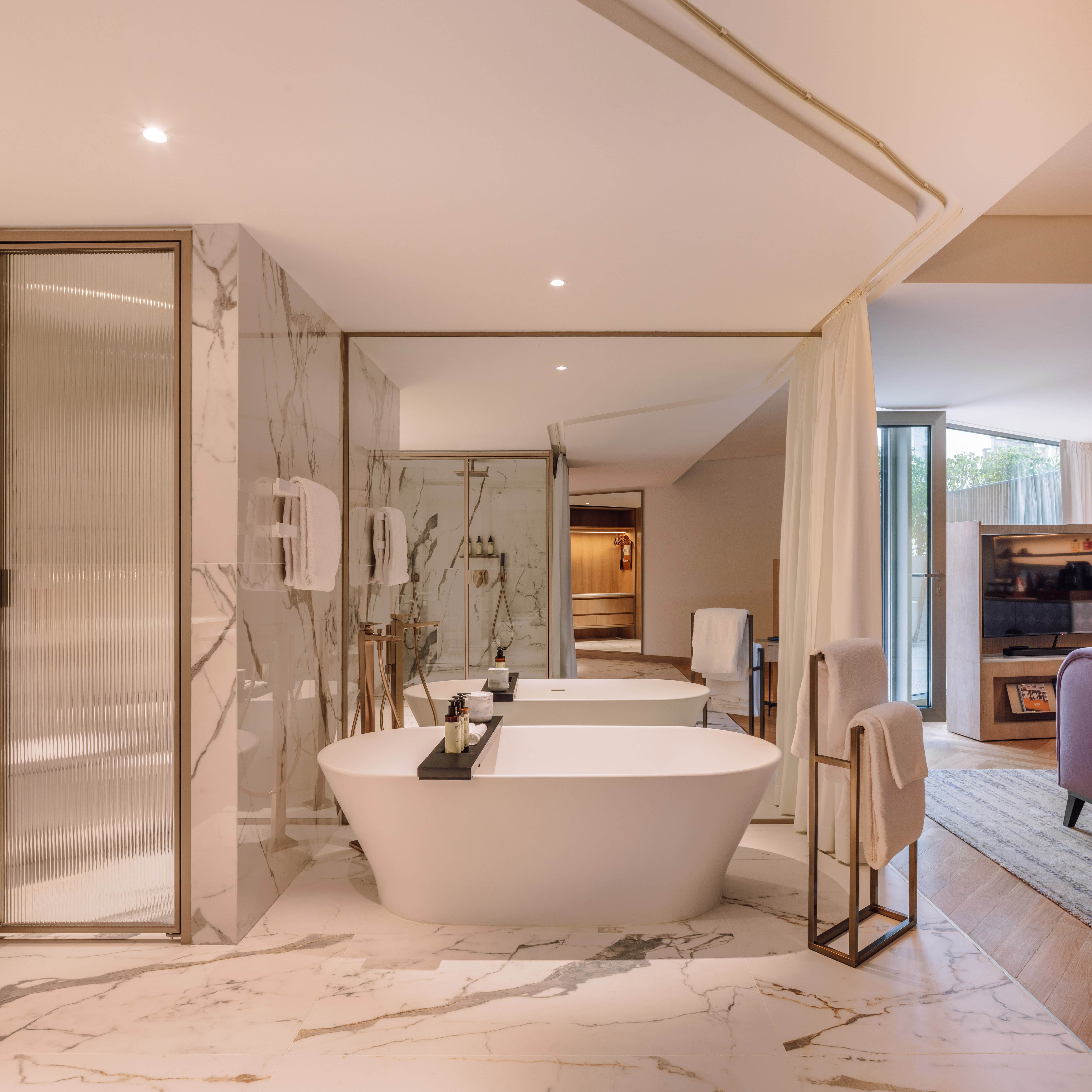 Luxury bathroom with freestanding tub, marble walls, glass shower, and gold accents.