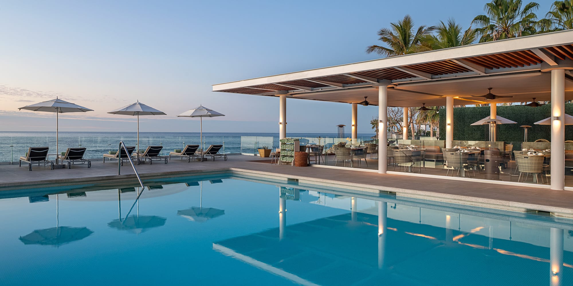 a pool with chairs and umbrellas by the ocean
