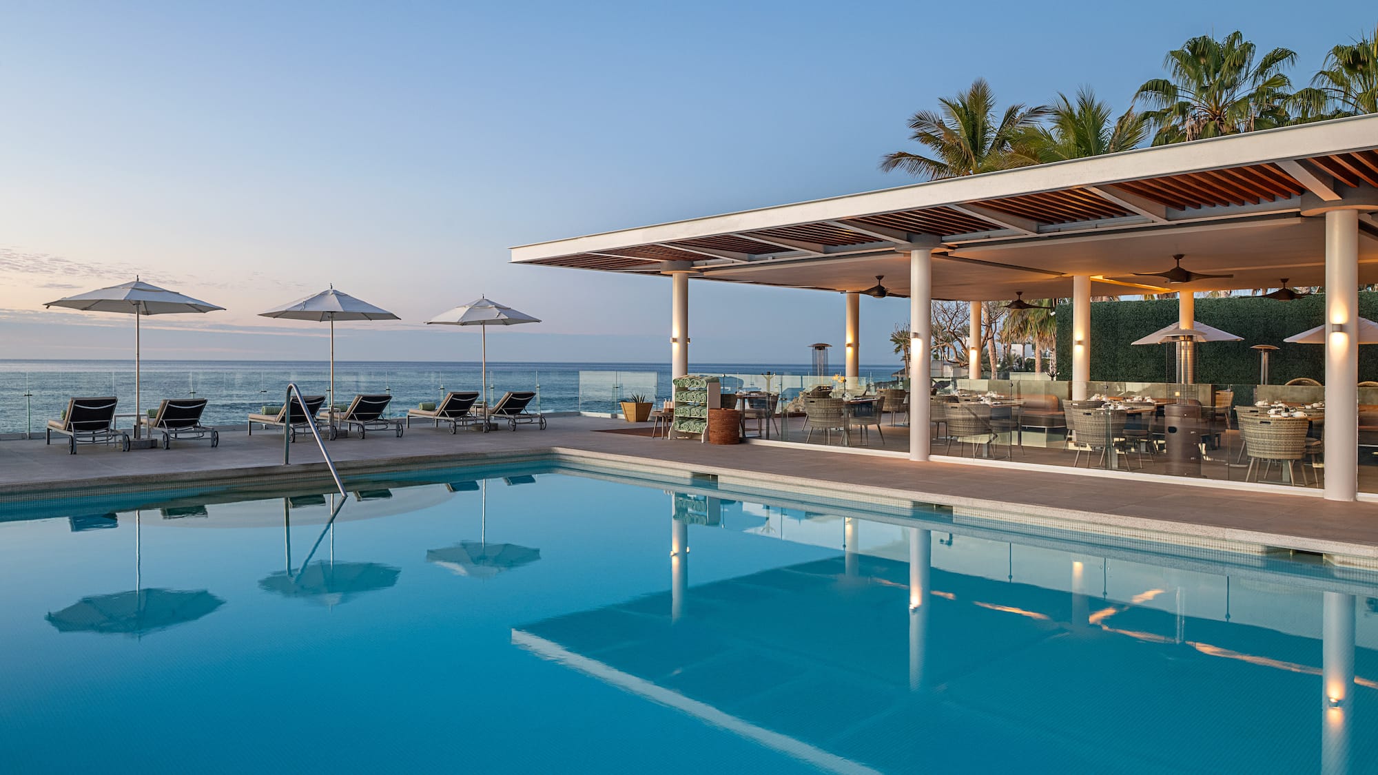 a pool with chairs and umbrellas by the ocean