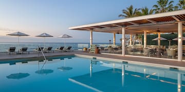 a pool with chairs and umbrellas by the ocean