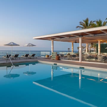a pool with chairs and umbrellas by the ocean
