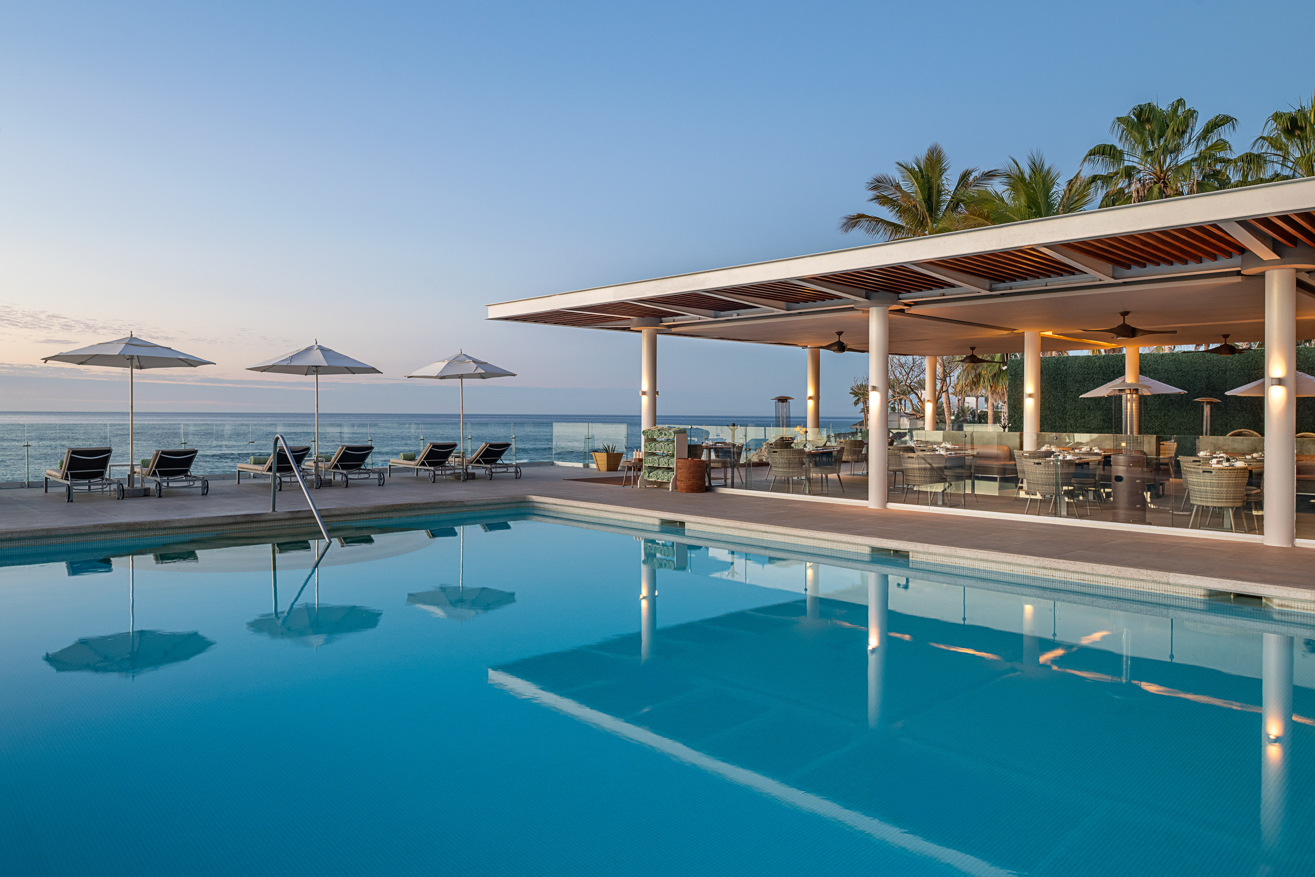 Oceanfront resort pool and modern outdoor restaurant at dusk.