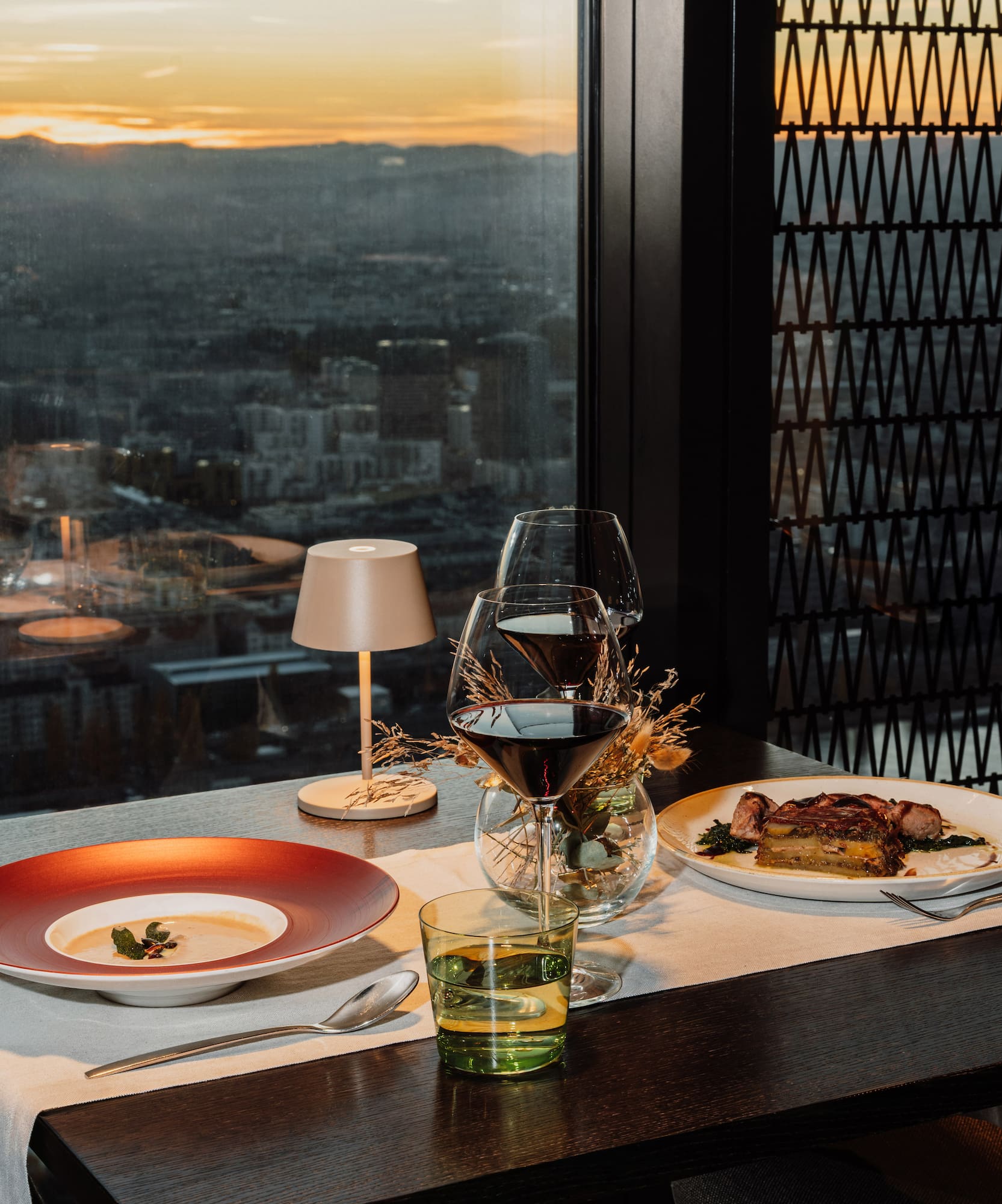 a table with plates and glasses on it and a table lamp and a city view