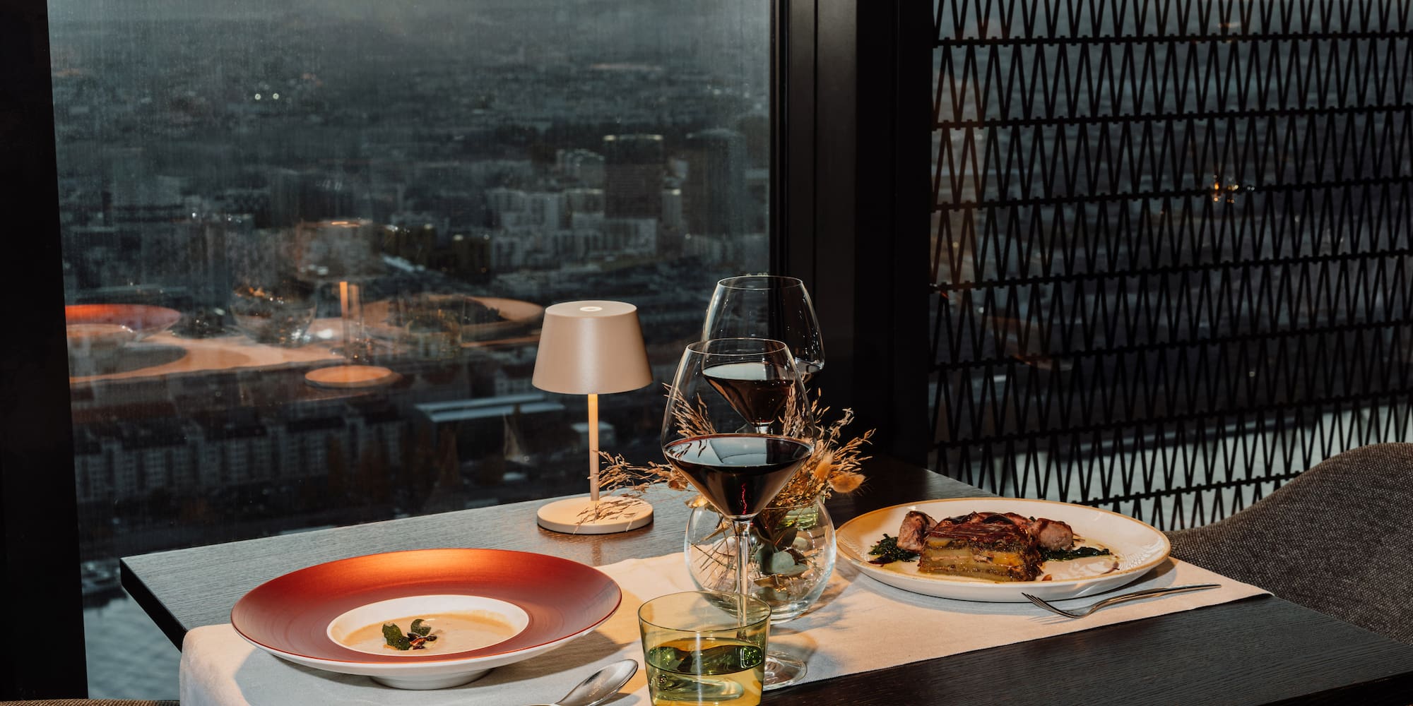 a table with plates and glasses on it and a table lamp and a city view
