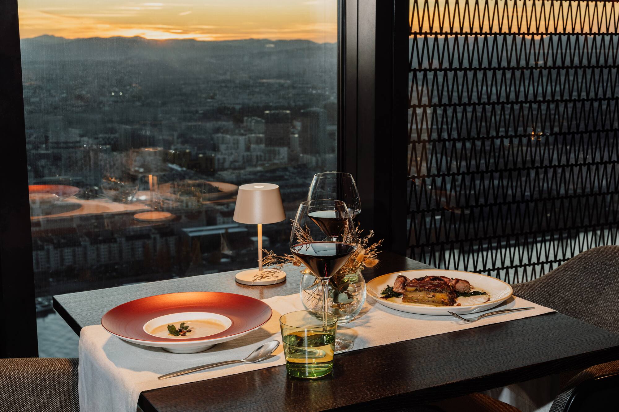 Restaurant dinner with soup, entree, wine, and city sunset view.