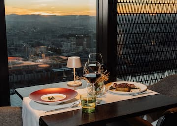 a table with plates and glasses on it and a table lamp and a city view