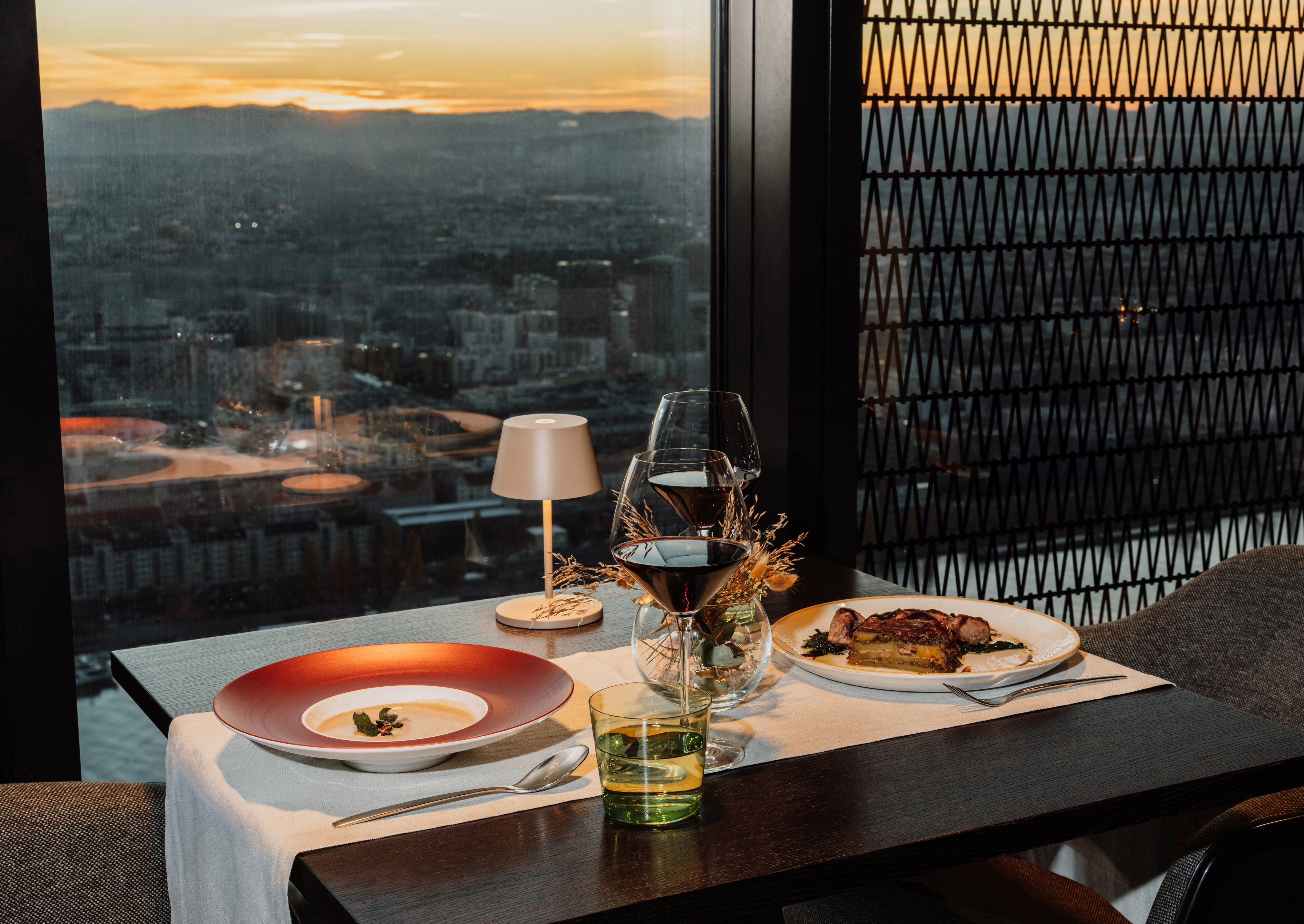 Restaurant dinner with soup, entree, wine, and city sunset view.