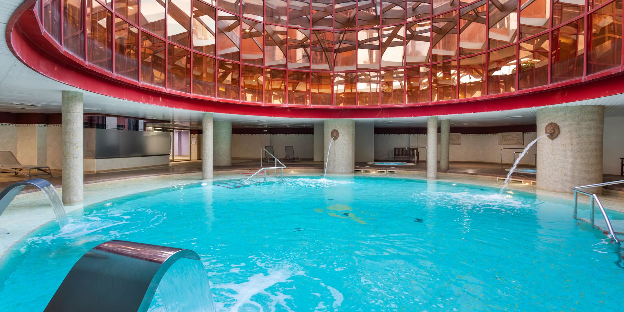 Indoor thermal spa pool with glass dome ceiling and waterfall features.