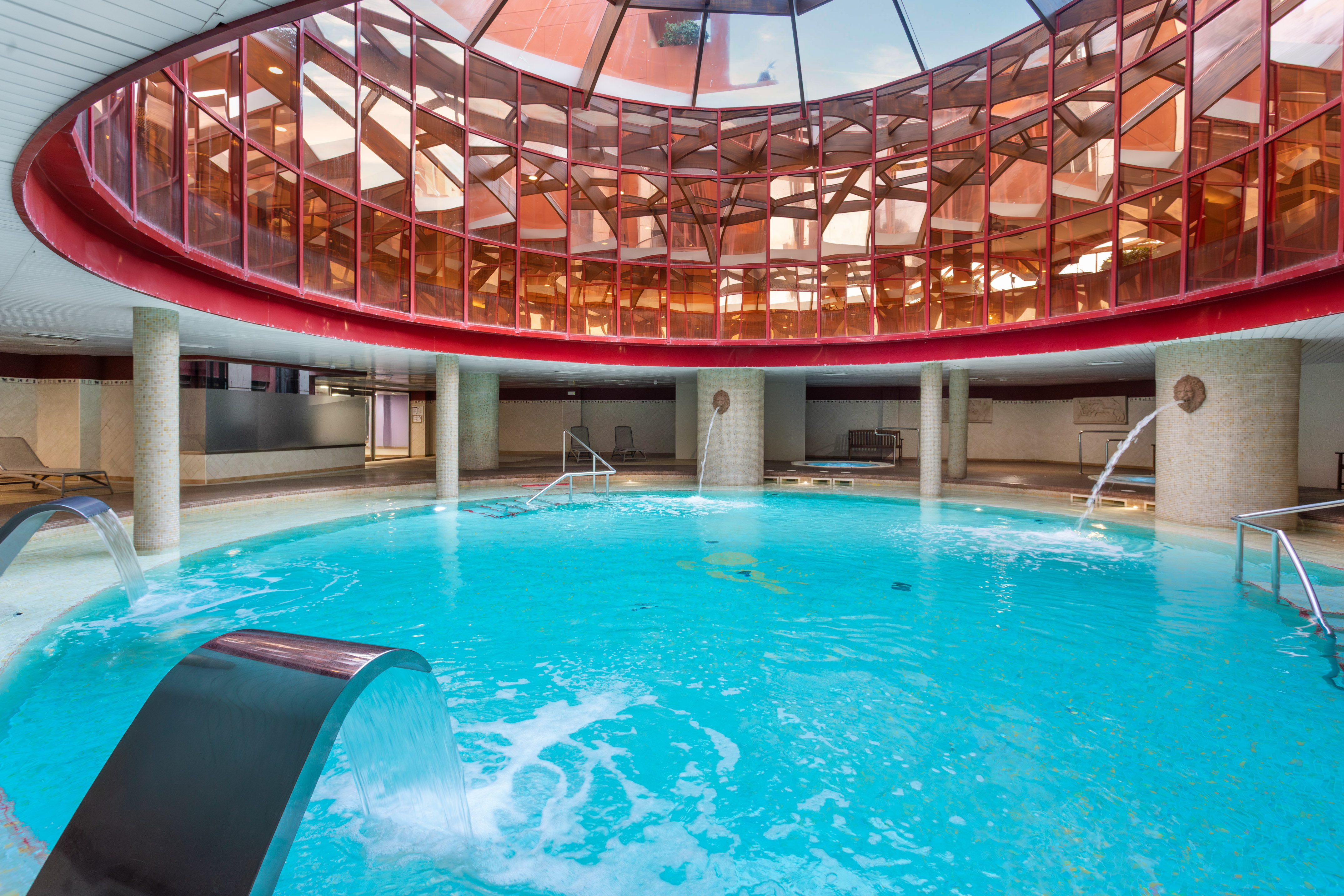 Indoor thermal spa pool with glass dome ceiling and multiple water jets.