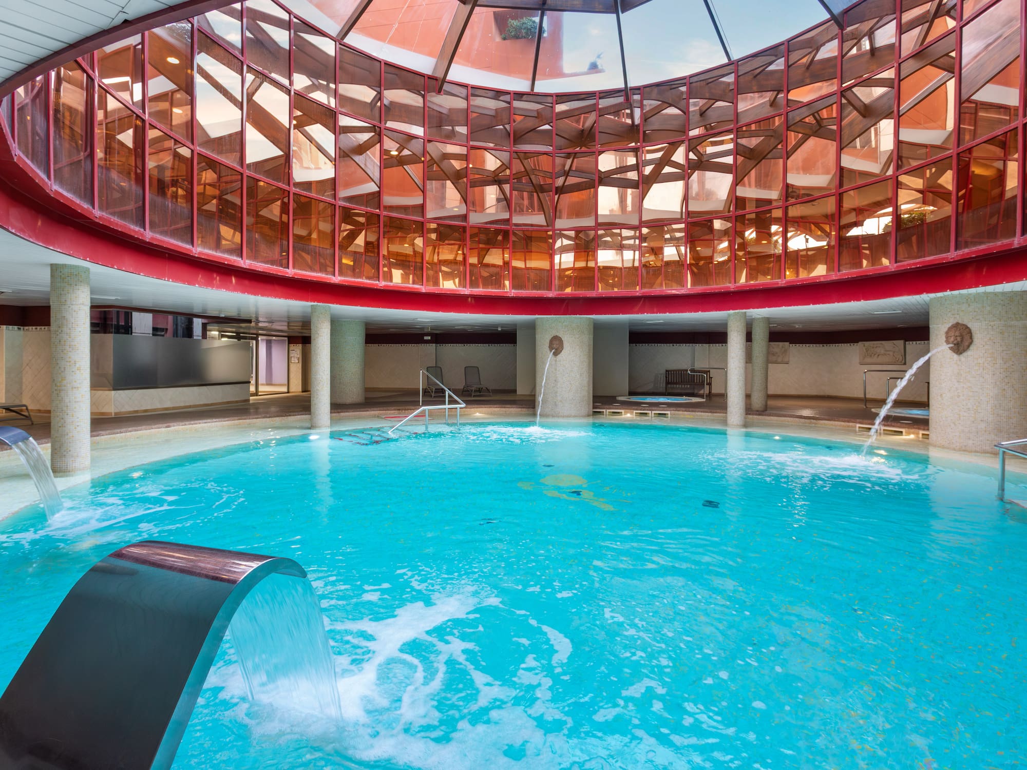 Indoor thermal spa pool with glass dome ceiling and multiple water jets.