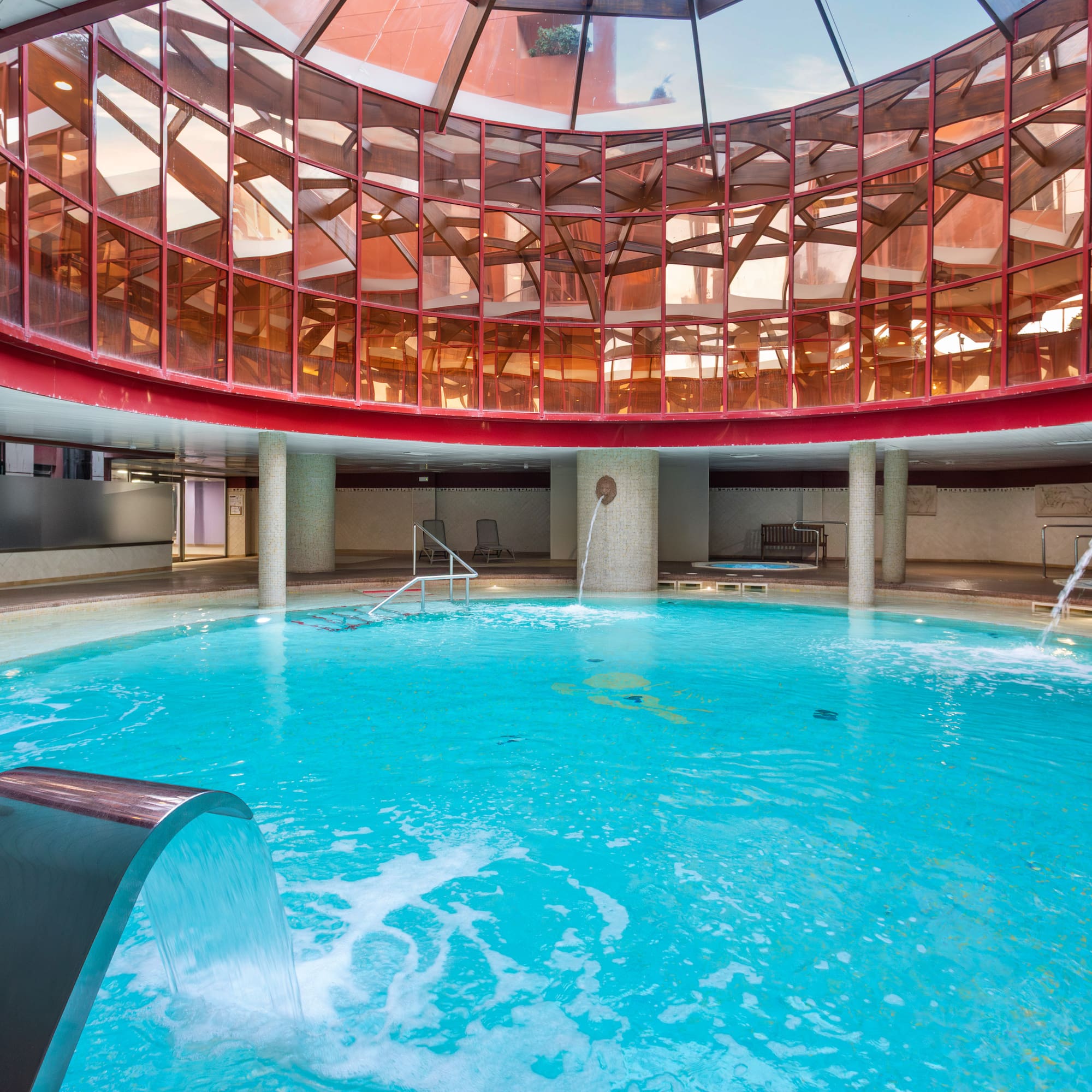 Indoor spa pool with hydrotherapy, waterfalls, and a glass dome ceiling.