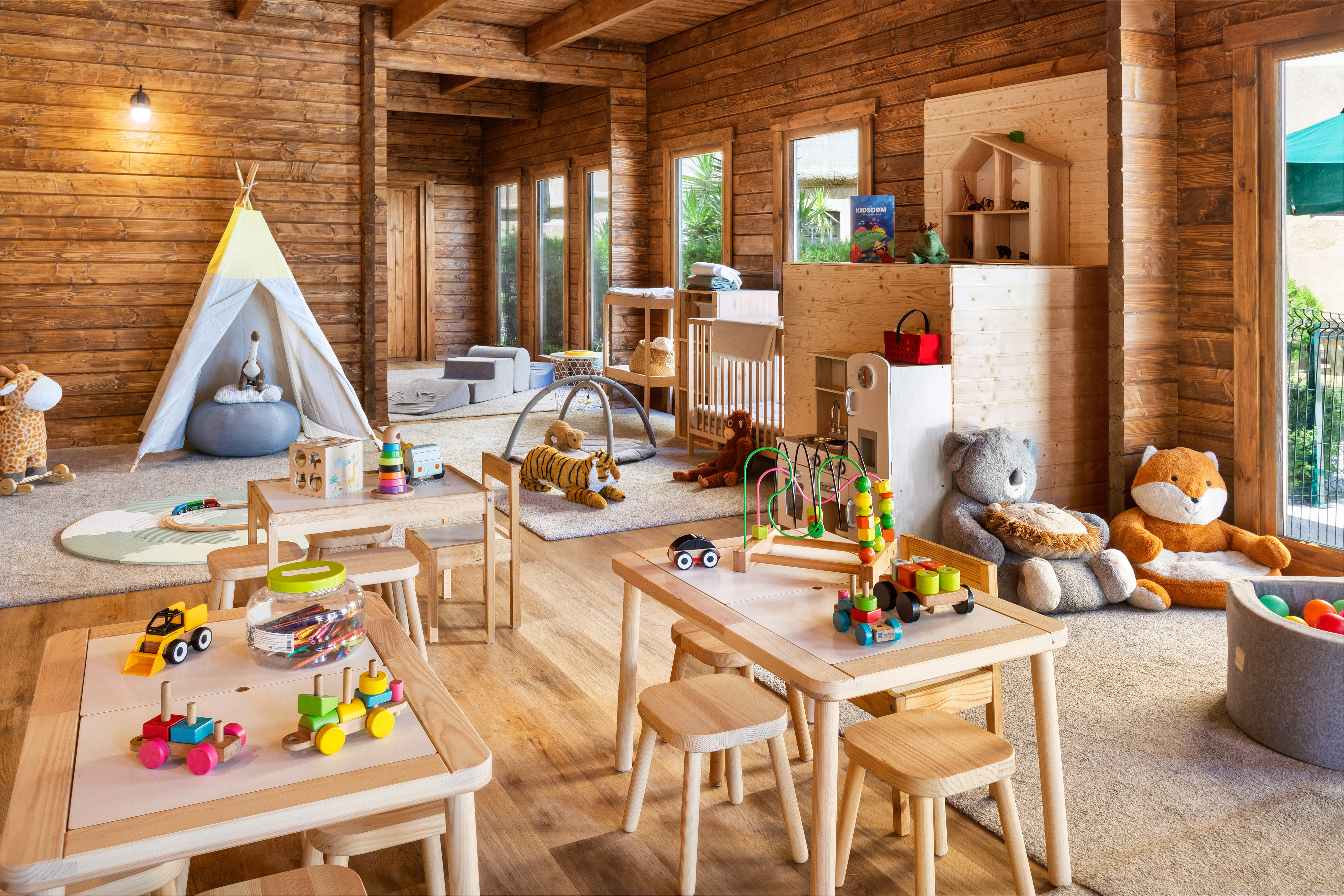 Wooden kids' playroom with colorful toys, small tables, and cozy play zones.