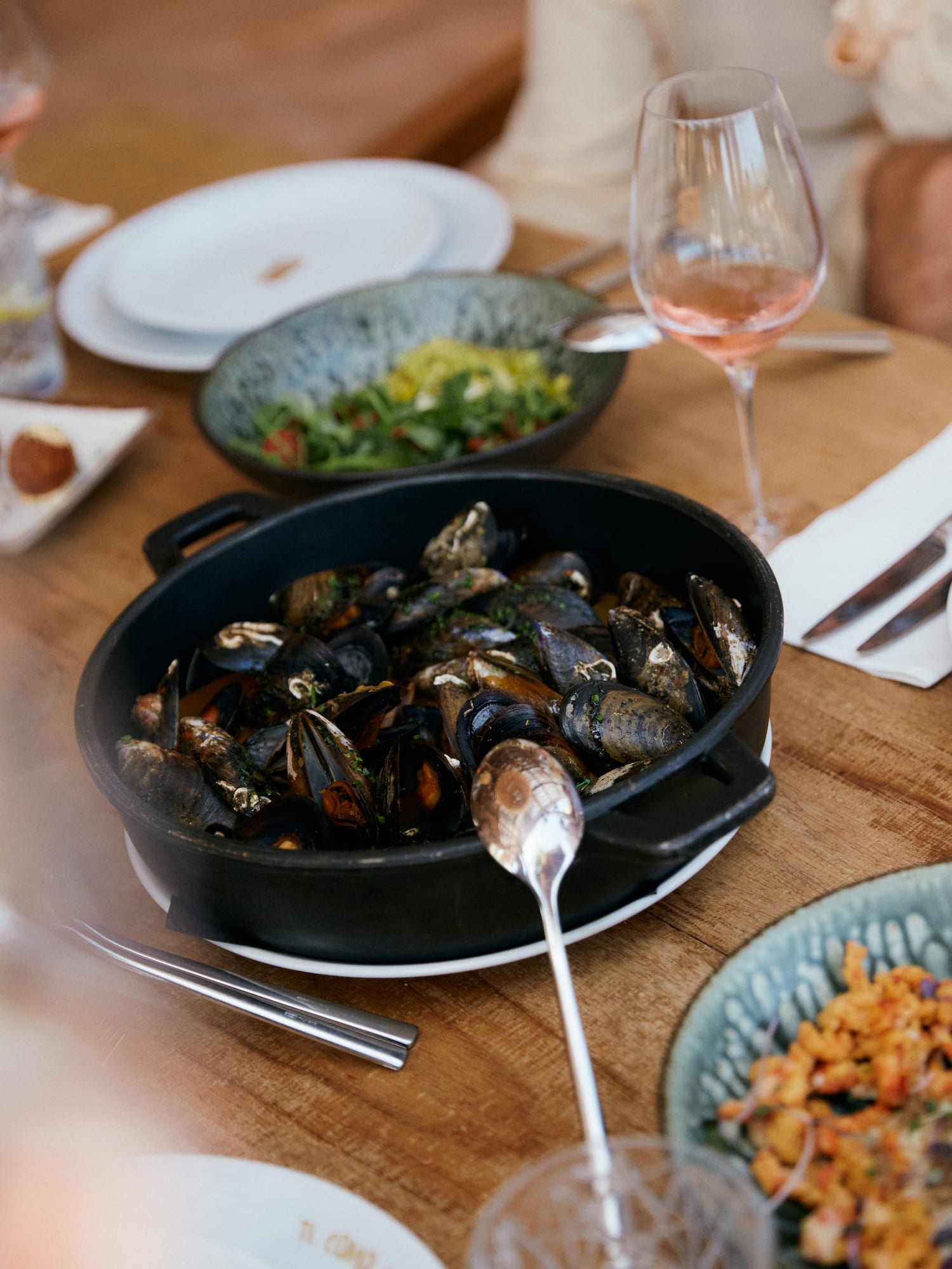 a bowl of mussels on a table with plates of food and wine