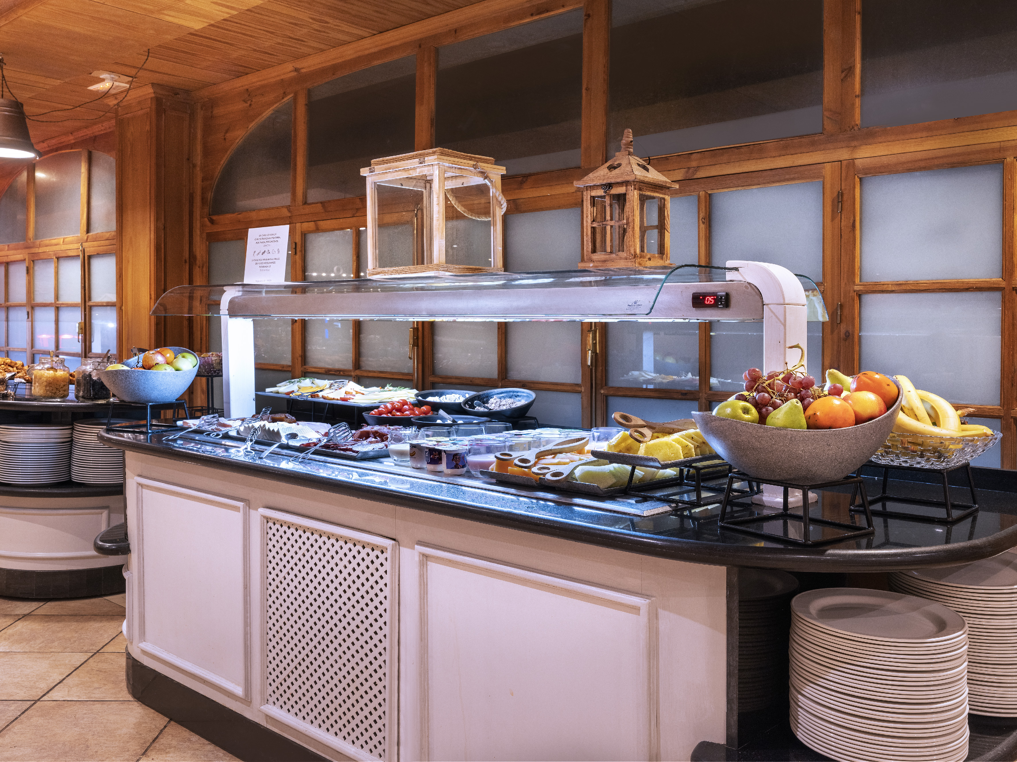 Breakfast buffet with fresh fruit, cold cuts, and yogurt in a hotel restaurant.