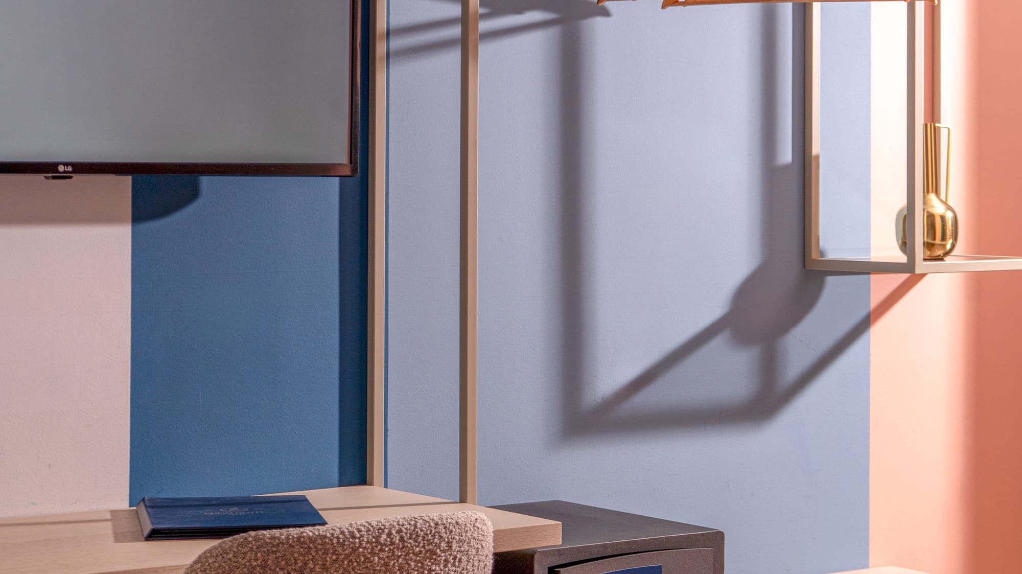 Modern hotel room interior: desk, TV, open wardrobe with hangers, and safe.