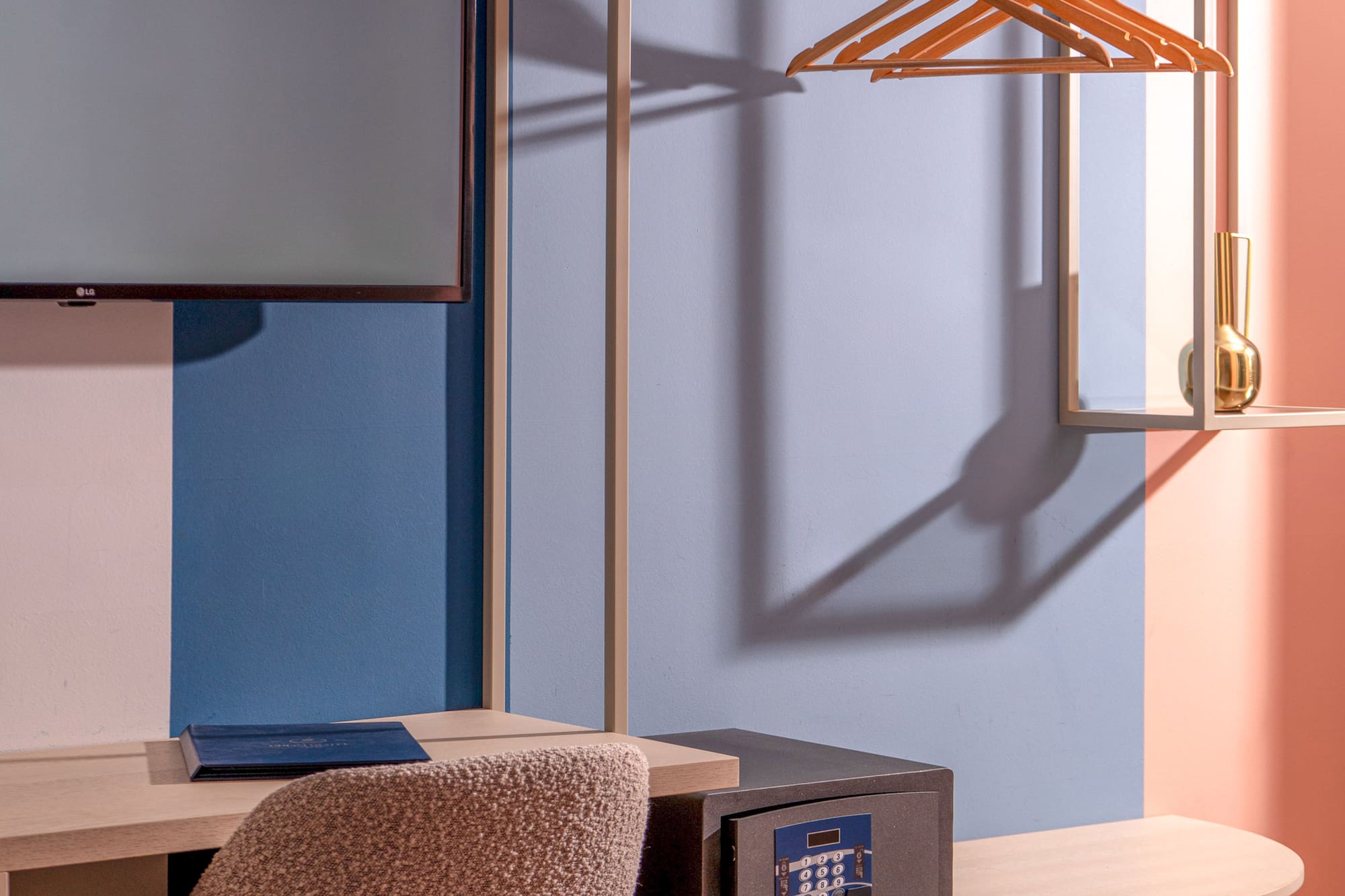 Modern hotel room interior: desk, TV, open wardrobe with hangers, and safe.